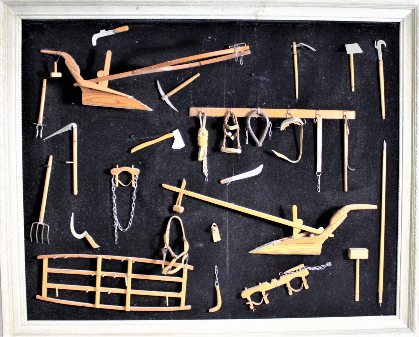 This framed collection of over two dozen handcrafted miniature antique farm implements are all unsigned, but presumed to have been made in Canada in circa 1969 in a Folk Art style. The implements are hand carved and handcrafted of wood and leather