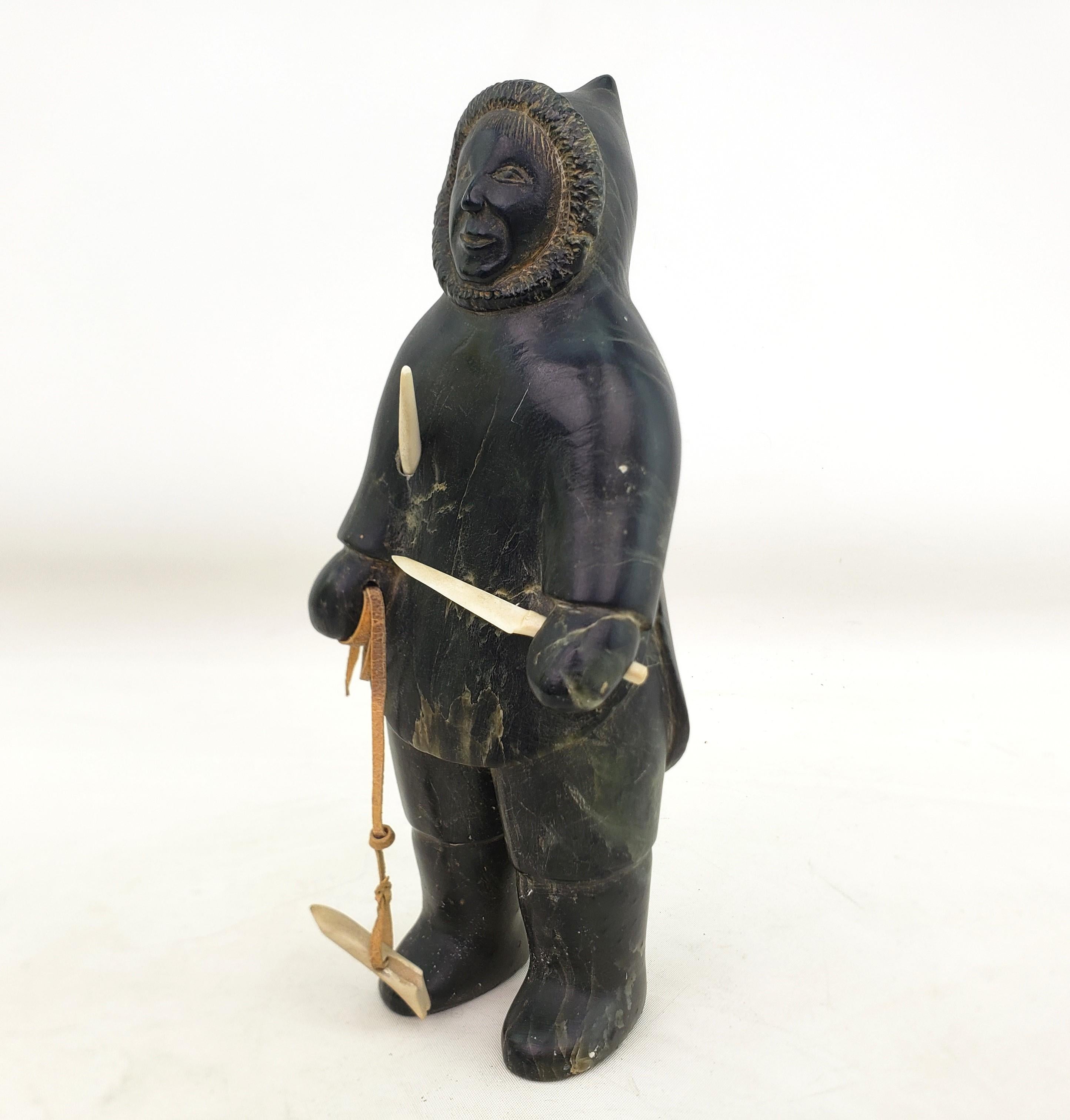 This well executed sculpture is signed by an unknown artist and originated from Canada and dates to approximately 1960 and done in the Mid-Century Inuit style. The sculpture is composed of soapstone and depicts an Inuit hunter with a spear and knife