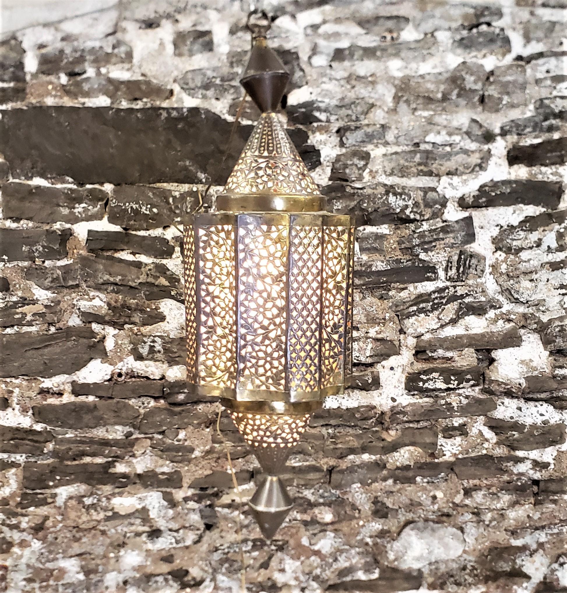 This lantern is swag lamp is unsigned, but originated from Morocco and dates to approximately 1965 and done in the period Mid-Century Modern style. The lantern is composed of brass sheeting which has been shaped and pierced with geometric designs.