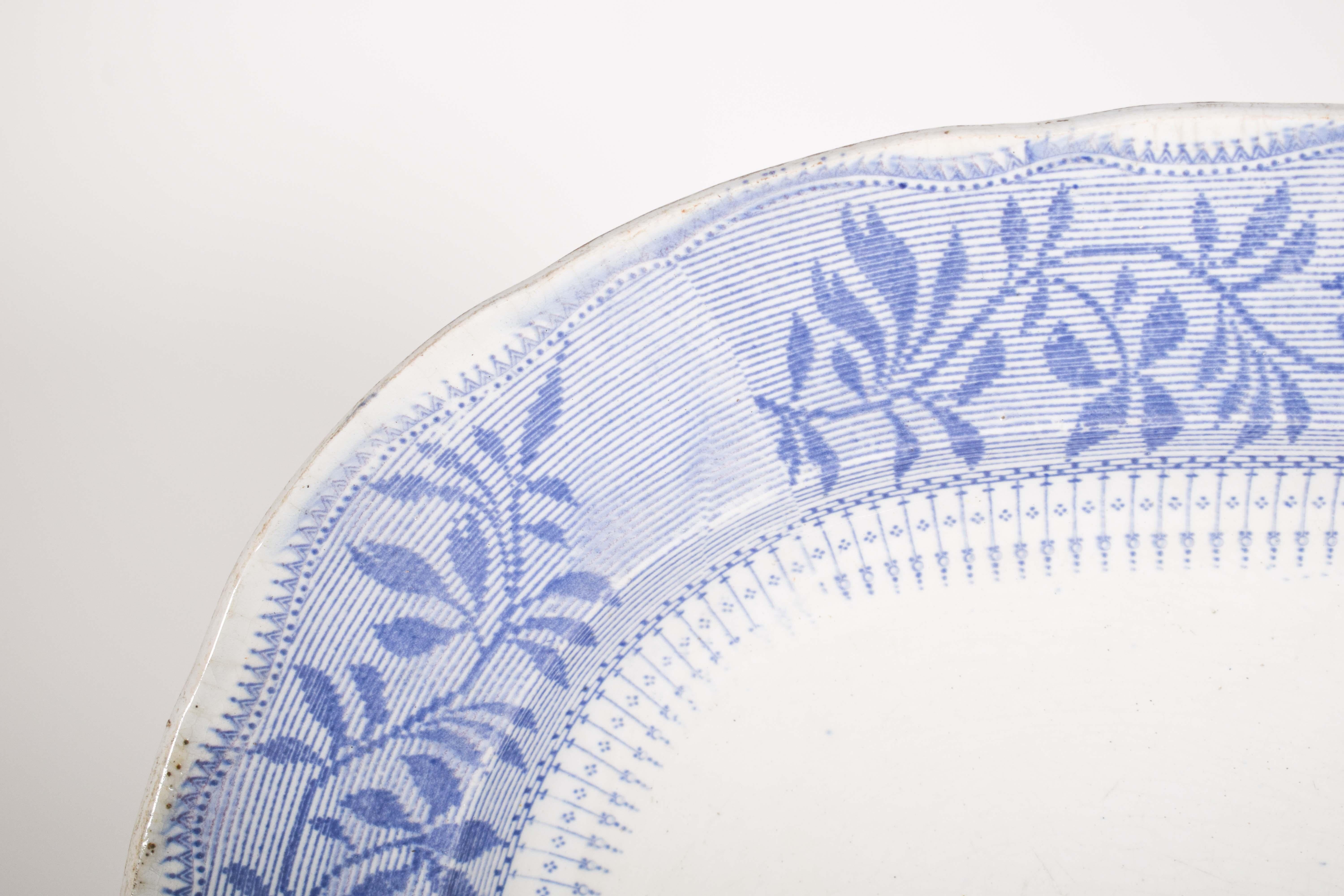 European porcelain dish, oval in shape and with slightly wavy edges. Decorated in blue on a white background, the center stands out with a bucolic scene depicted in soft tones. Two swans swim serenely on a lake, while two ducks take off, surrounded