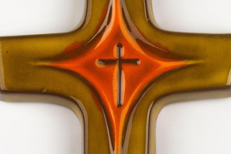 Midcentury European ceramic wall cross in olive green and orange. From a large collection of crosses handmade by Flemish artisans.

From modernism to brutalism, the crosses in our collection range from being as Futurist as a modernist church to as