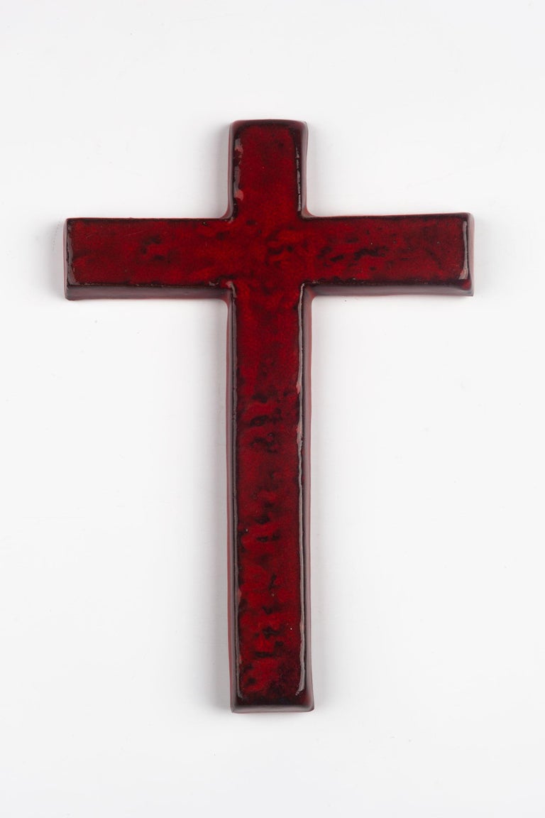 Midcentury European ceramic wall cross in red glazed ceramic and with black textural details in and around the border of the cross. From a large collection of crosses handmade by Flemish artisans. 

From modernism to brutalism, the crosses in our