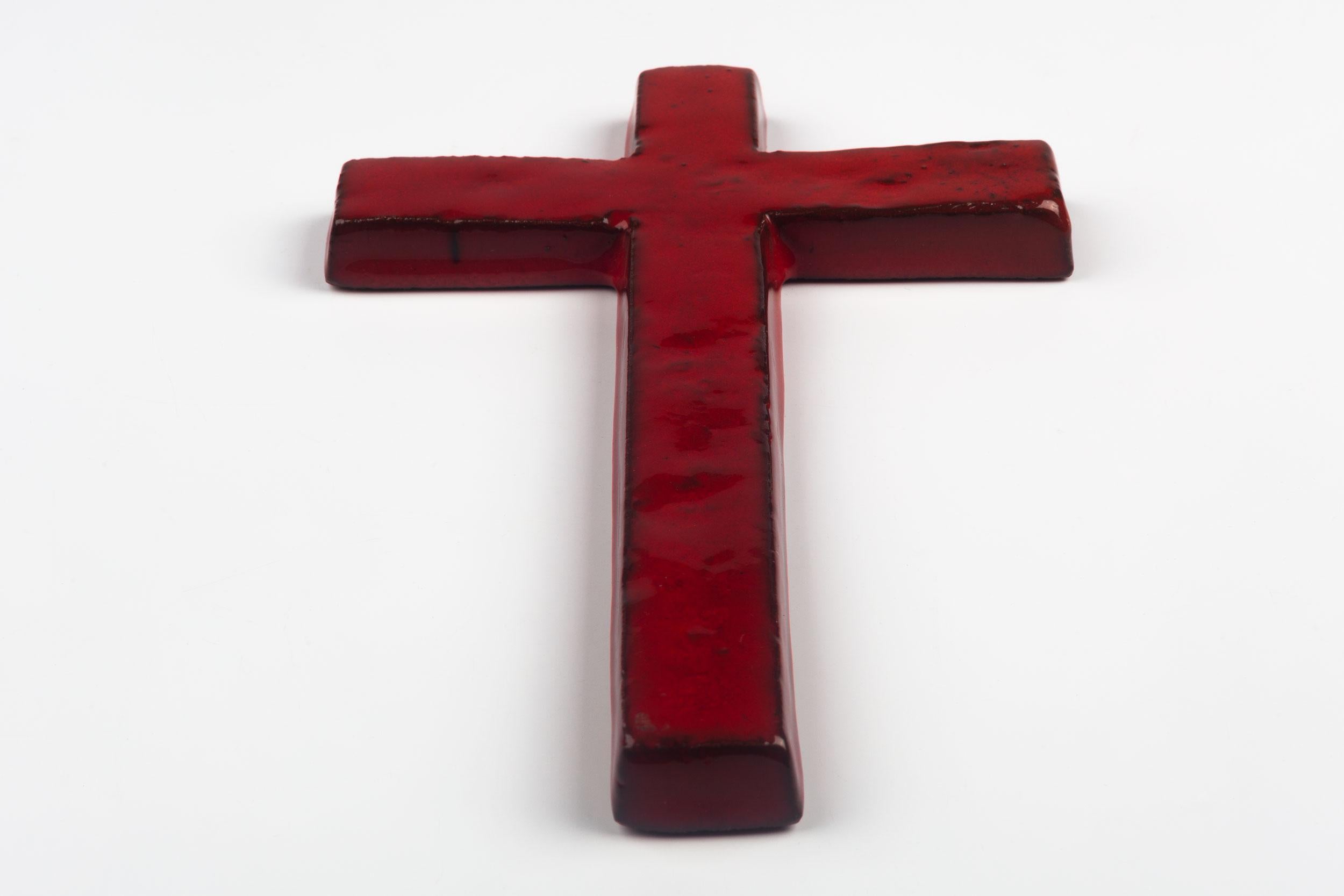 Midcentury European ceramic wall cross in red glazed ceramic and with black textural details in and around the border of the cross. From a large collection of crosses handmade by Flemish artisans. 

From modernism to brutalism, the crosses in our