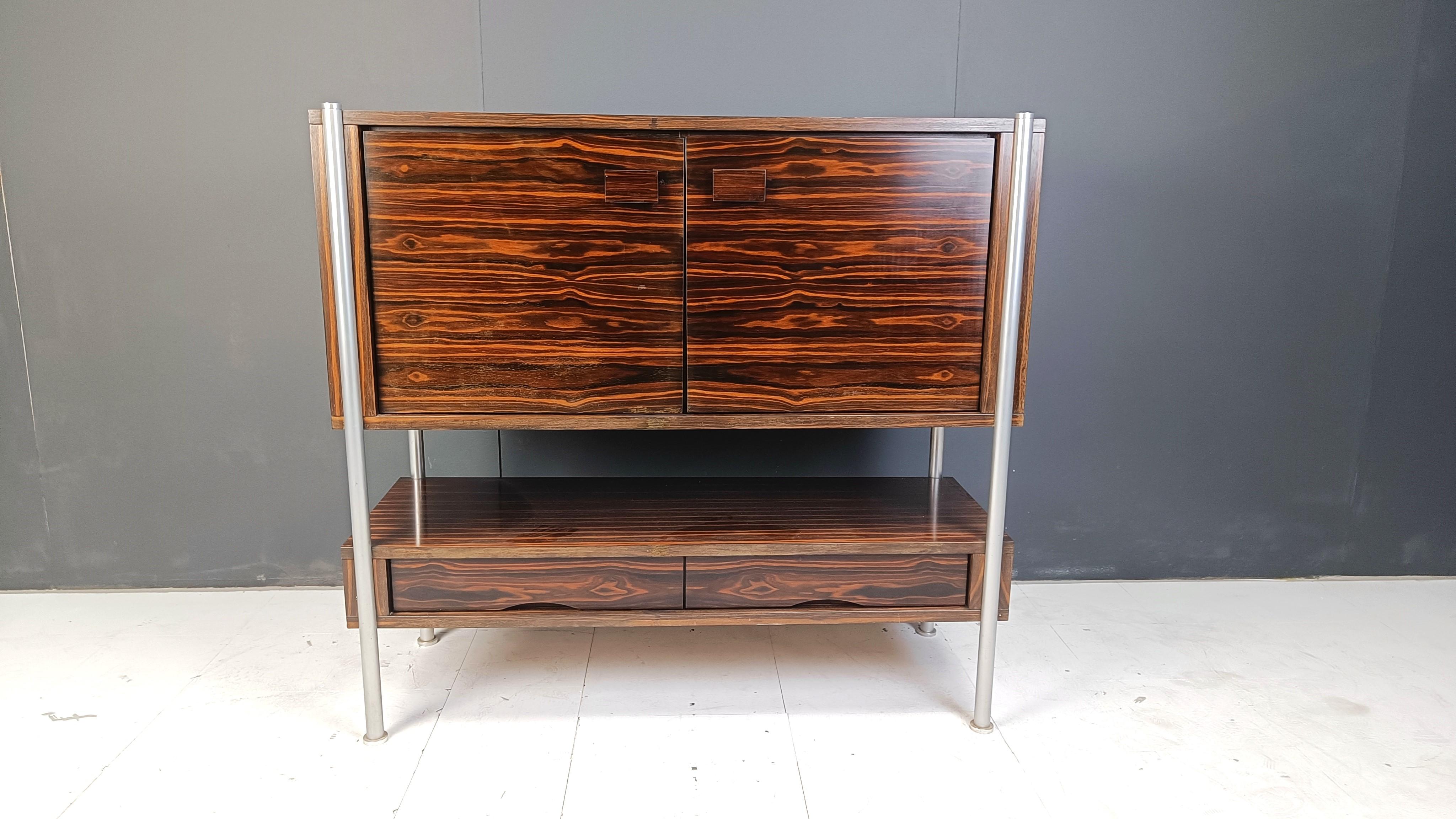 Mid century bar cabinet made from exotic wood veneer.

Beautiful natural wood veining.

2 doors and two drawers, mirrored bar compartment with a glass shelve.

1960s - Belgium

Good condition

Dimensions:
Height: 128cm
Width: 135cm
Depth: