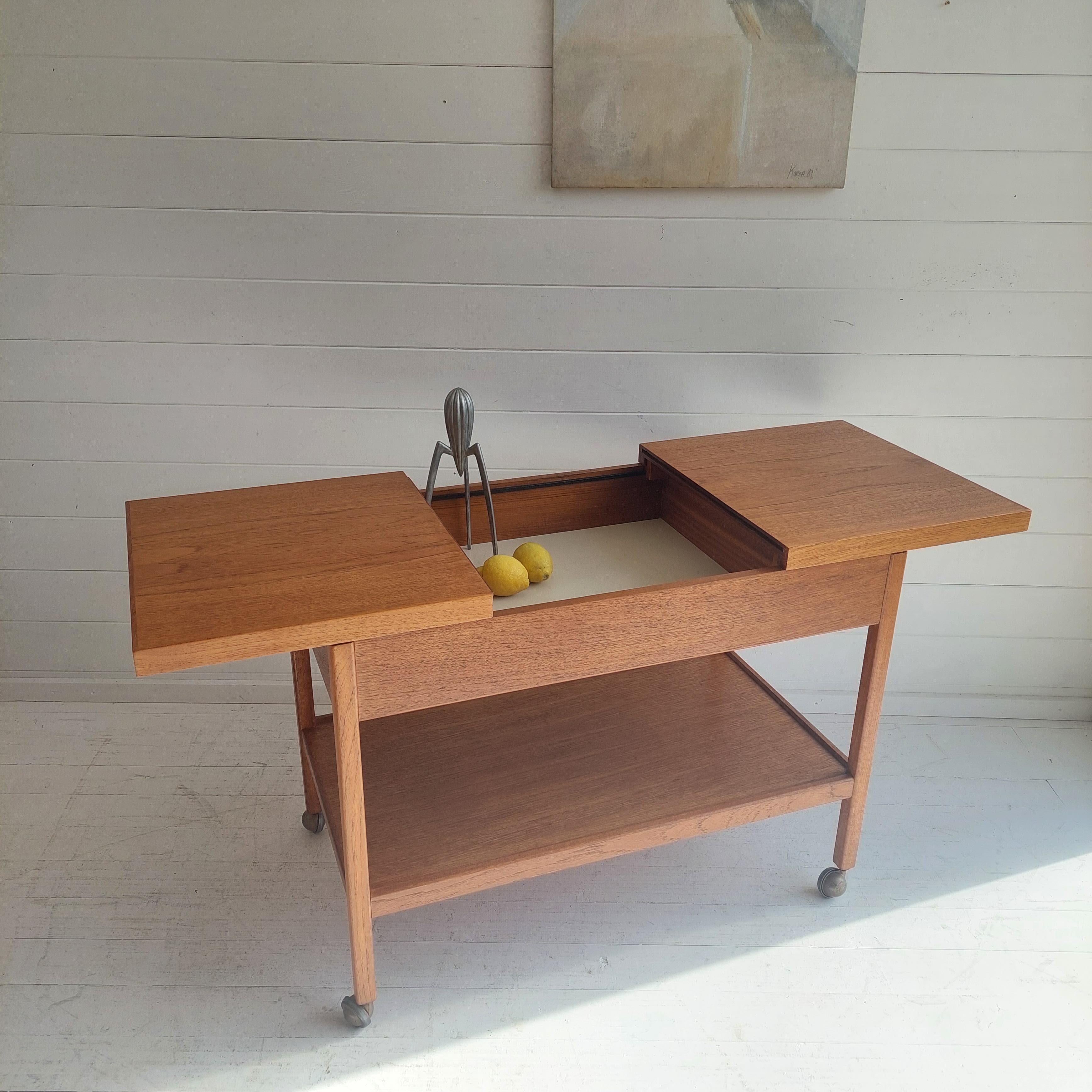 Vintage 1960/70s serving/bar 2 tier cart with sliding tops and internal compartment by 
Under Hans Jørgen Wegner influence Denmark. 
Due its lines and use of white formica it might was manufactured by Remploy. Sadly no makers to confirm.

A
