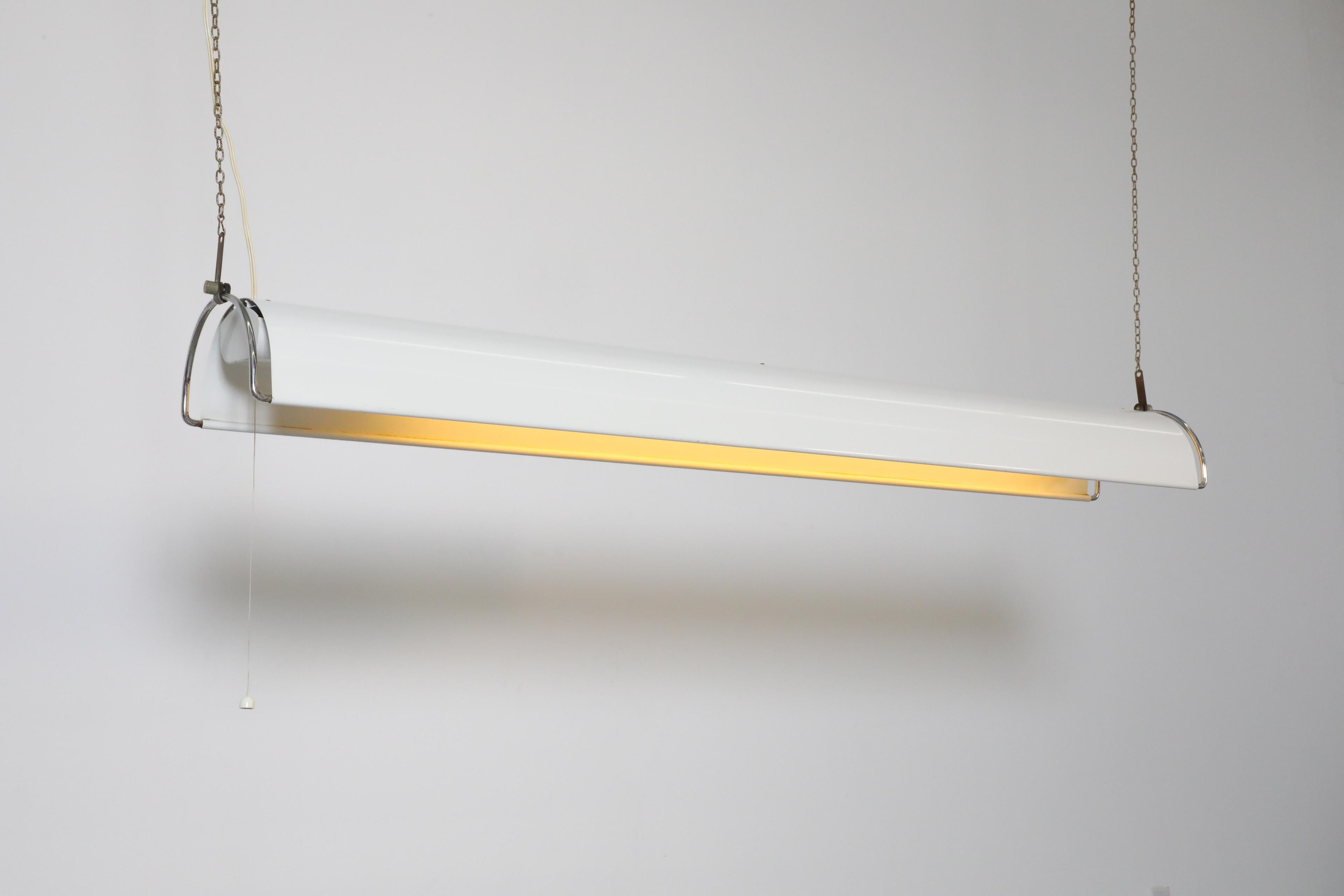 Vintage, Fagerhult manufactured, industrial hanging shop lamp with white enameled curved shade, chrome frame and long fluorescent bulb. The lamp hangs suspended from two chains and has a decorative inner shade around the bulb. Operates with a pull