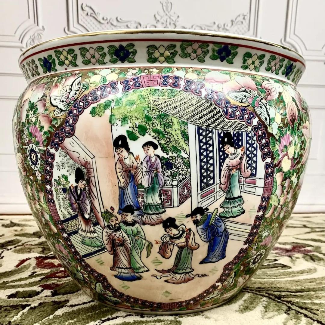 An elegant hand-painted porcelain fish bowl in the highly sought famille rose pattern featuring a traditional scene on either side and iconic symbolism throughout.  Exquisite detail, rich in texture, beautiful gilt accents. 

Made in China circa