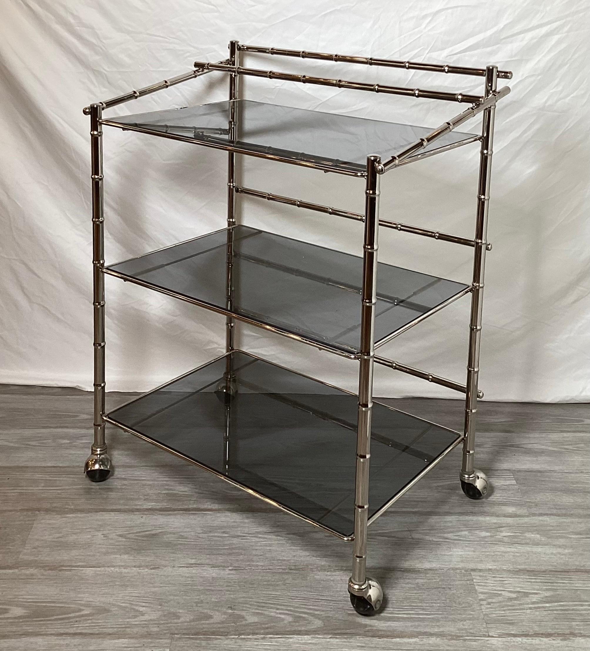 Very nice midcentury Faux bamboo chrome bar cart with smoked glass shelves.
Three tiered shelves with a bottle rack on the top shelf. The cart is in very good original condition.