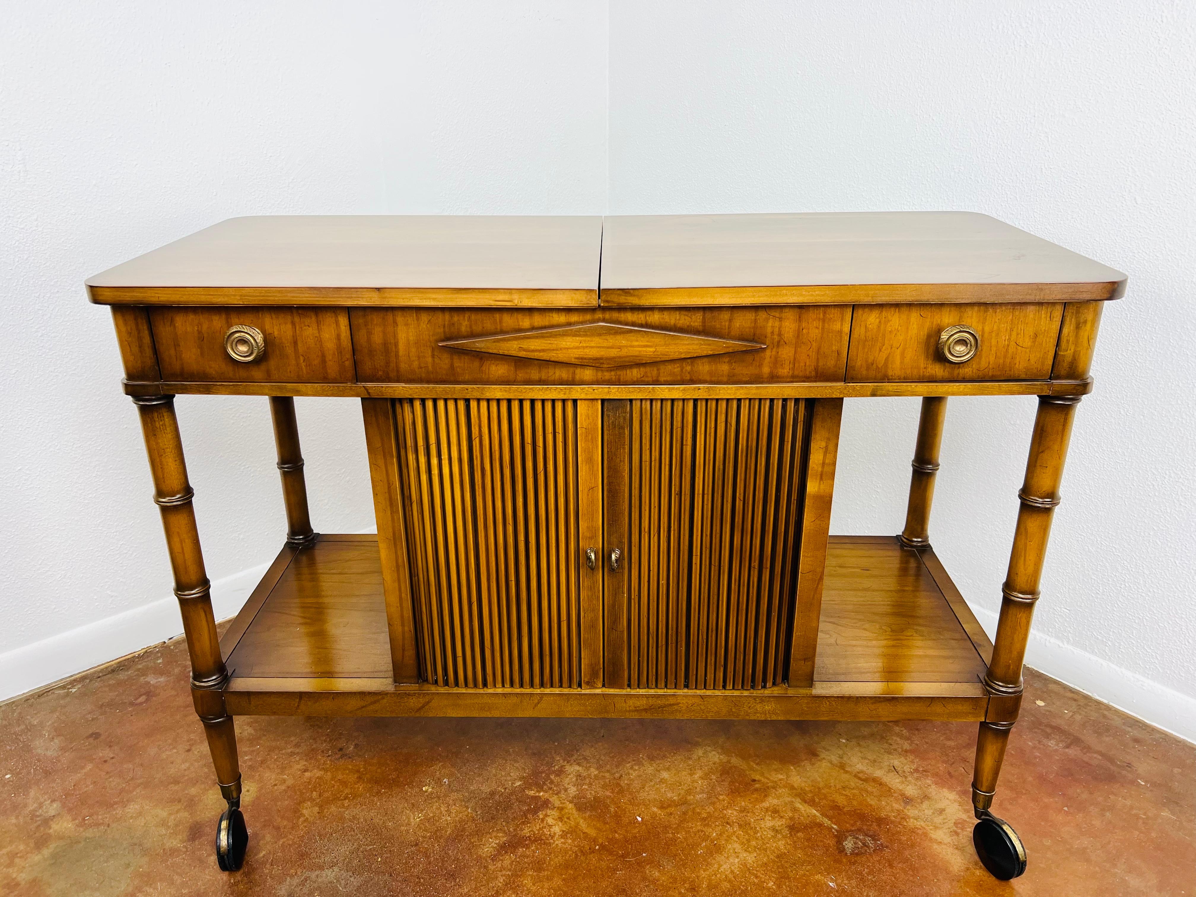Sophisticated mid-century rolling bar / server with expandable top and faux bamboo legs. Roll front Tambour doors. Heavy, solid wood construction.
