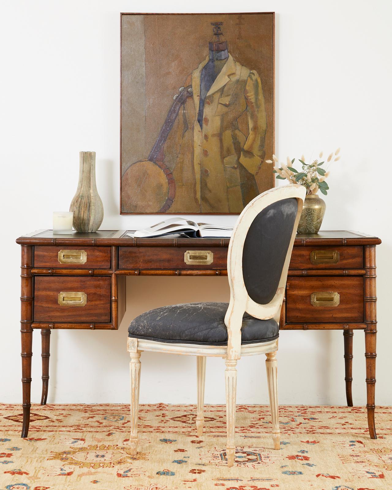 Distinctive Mid-Century Modern leather top writing table or desk by Drexel. Constructed from rich mahogany having faux bamboo legs and border trim. Fronted by five storage drawers fitted with Campaign style brass hardware pulls. The large writing