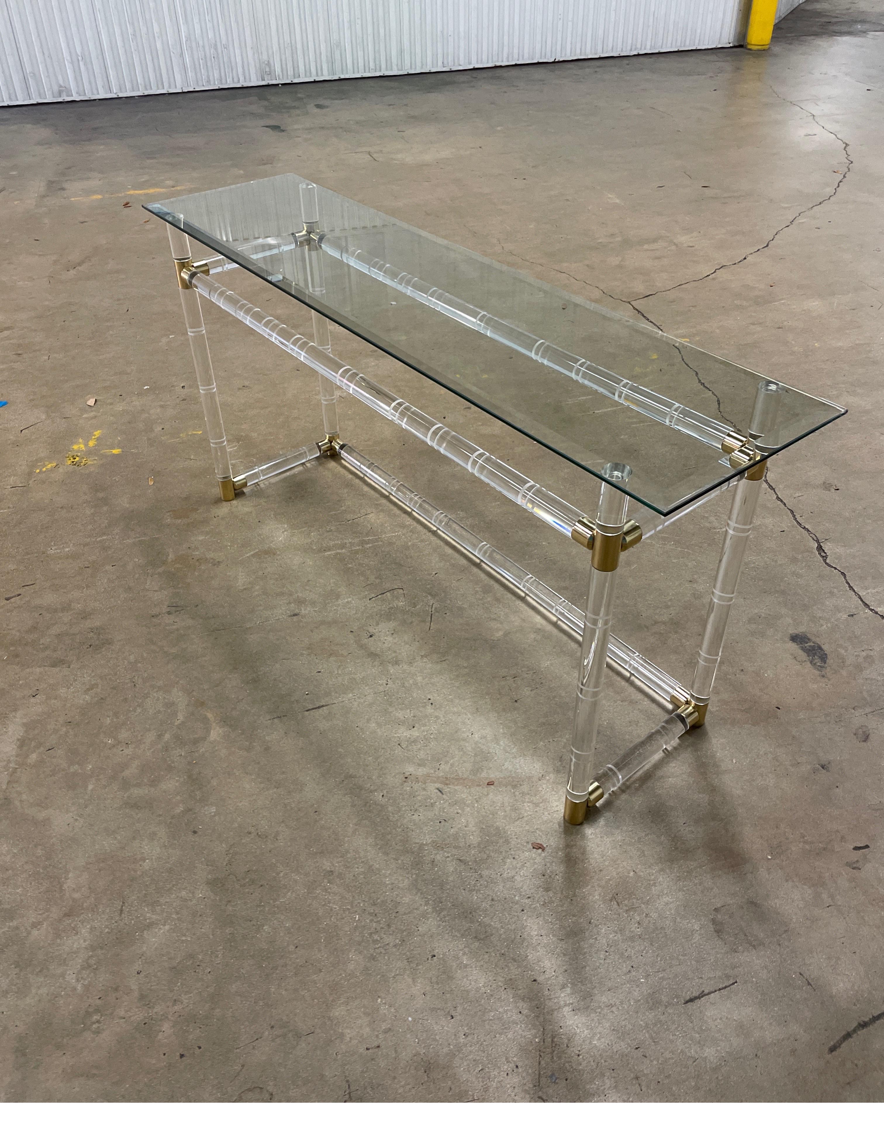 Vintage faux bamboo lucite and brass console table with beveled glass top. This Mid-Century Modern piece is designed to fit a pair of stools or bench underneath. A wonderful Hollywood Regency Mid-Century Modern piece in great condition.