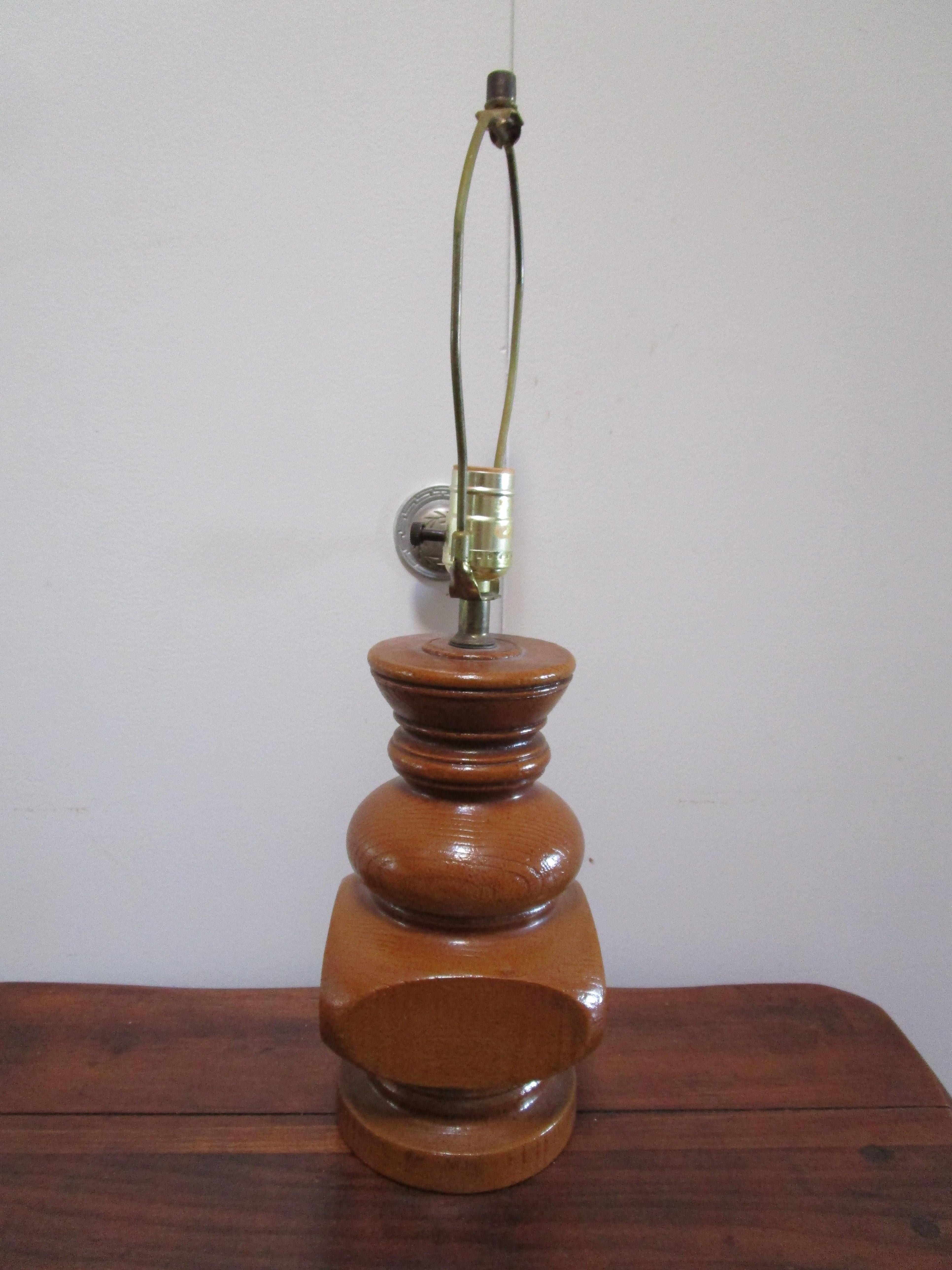 Le bloc de bois et l'aspect tourné de cette lampe ne sont qu'une illusion, car elle est fabriquée en poterie et non en bois. C'est tellement inhabituel. La silhouette, avec ses anneaux, ses chignons et ses blocs, est comparable aux tournures des