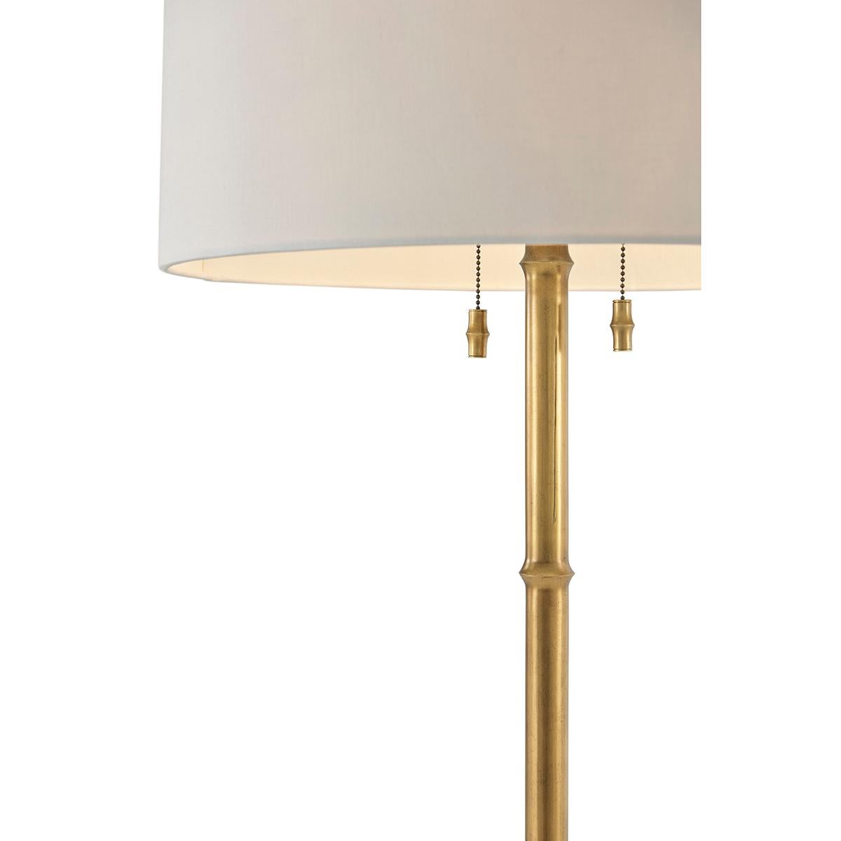 A mid-century chinoiserie-inspired floor lamp, with a round linen shade on a satin brass-finished faux bamboo pedestal and a disc base.

Dimensions: 23