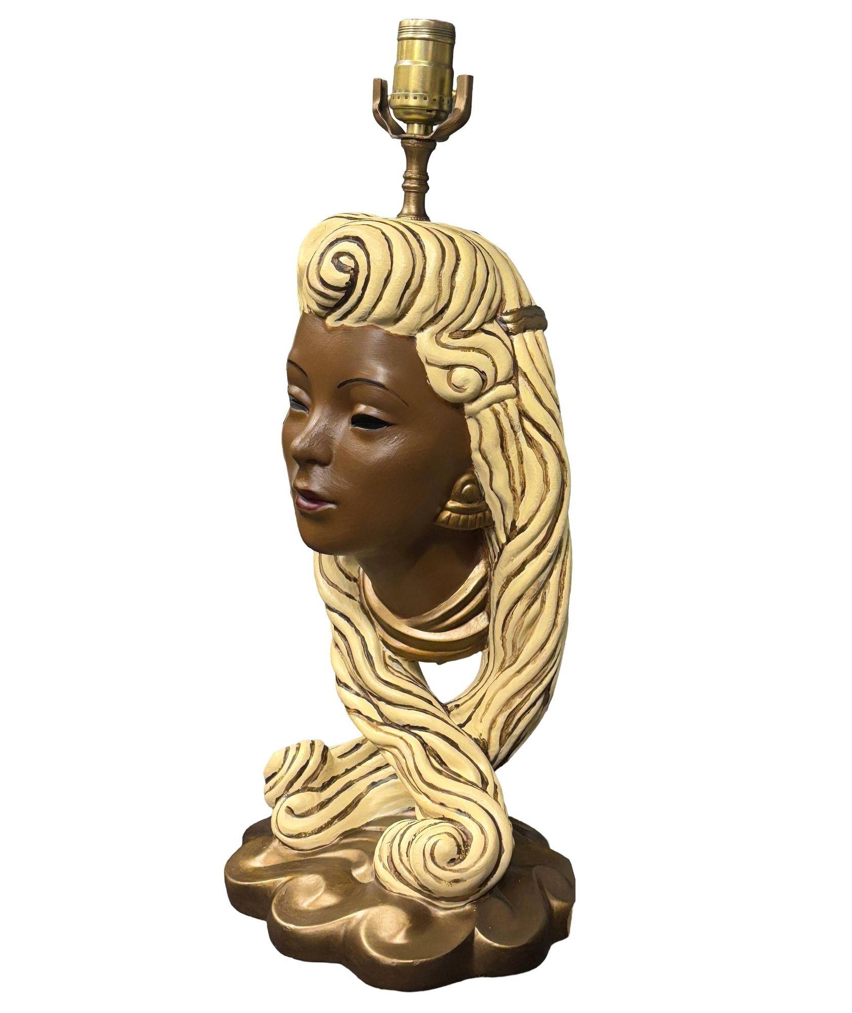 Questa lampada in gesso della metà del secolo scorso presenta un busto scultoreo dettagliato di una giovane donna polinesiana elegantemente acconciata con fluenti capelli biondi e accessori dorati. Vero e proprio tesoro vintage, la lampada cattura