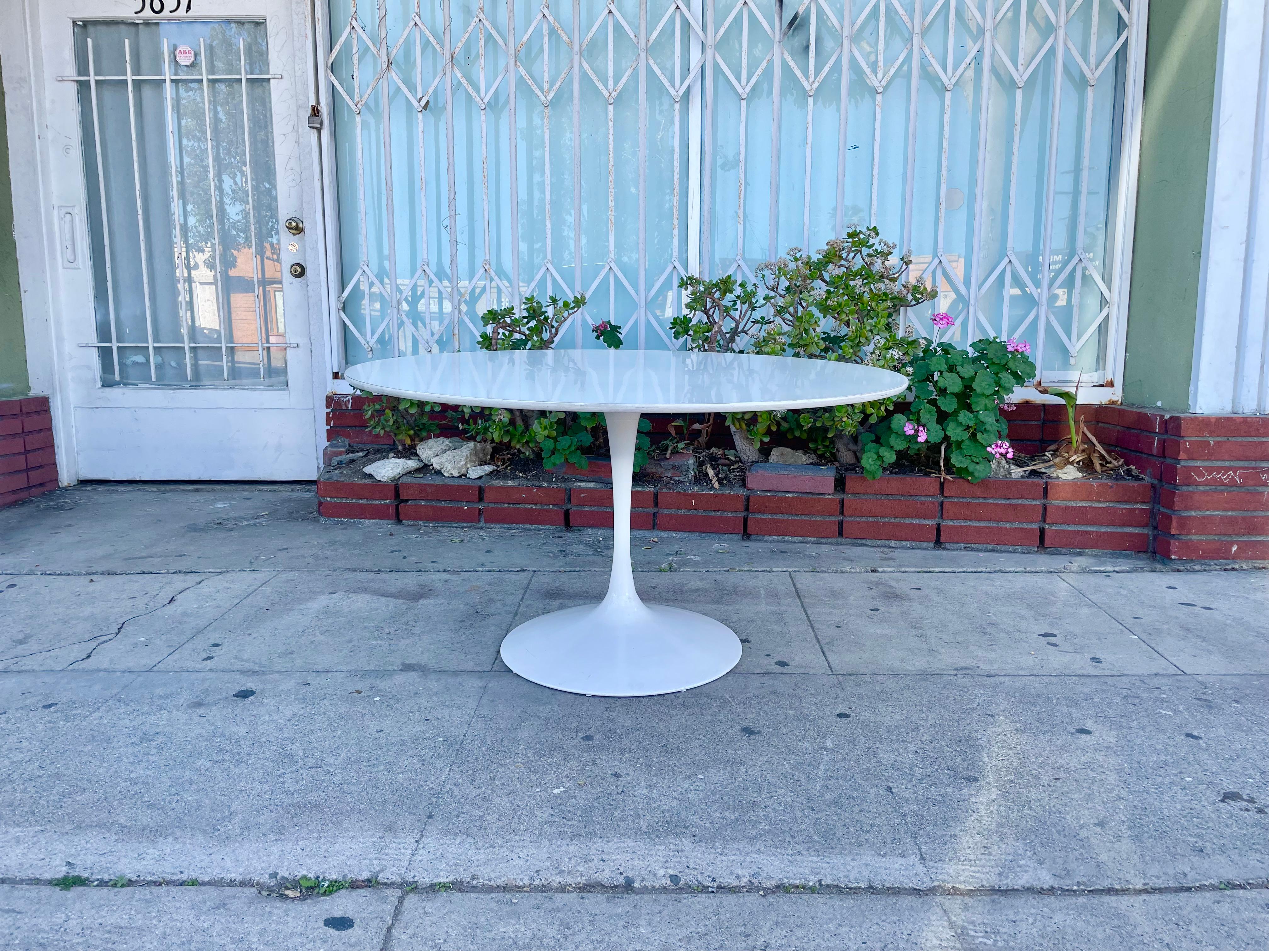 This beautiful Mid Century Fiberglass Dining Table Styled After Eero Saarinen features a round white wooden top with a cast iron metal base to support the top, giving the hourglass figure to it.