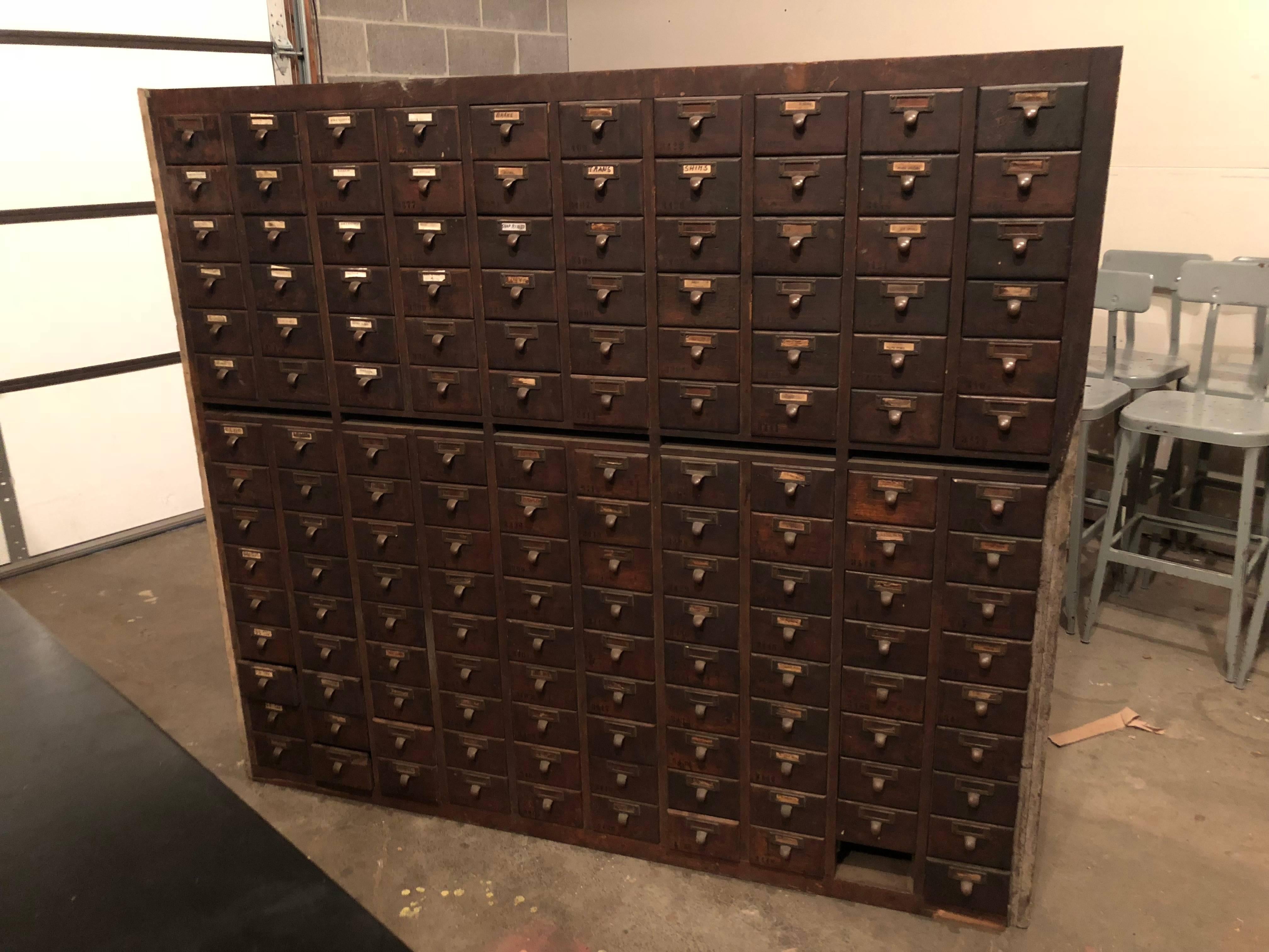 Midcentury file cabinet of oak, formerly used in library. Houses 150 sliding drawers with brass pulls. Ideal storage unit. Consists of two pieces, one stacked atop the other. Could be situated in two different locations to expand functionality.