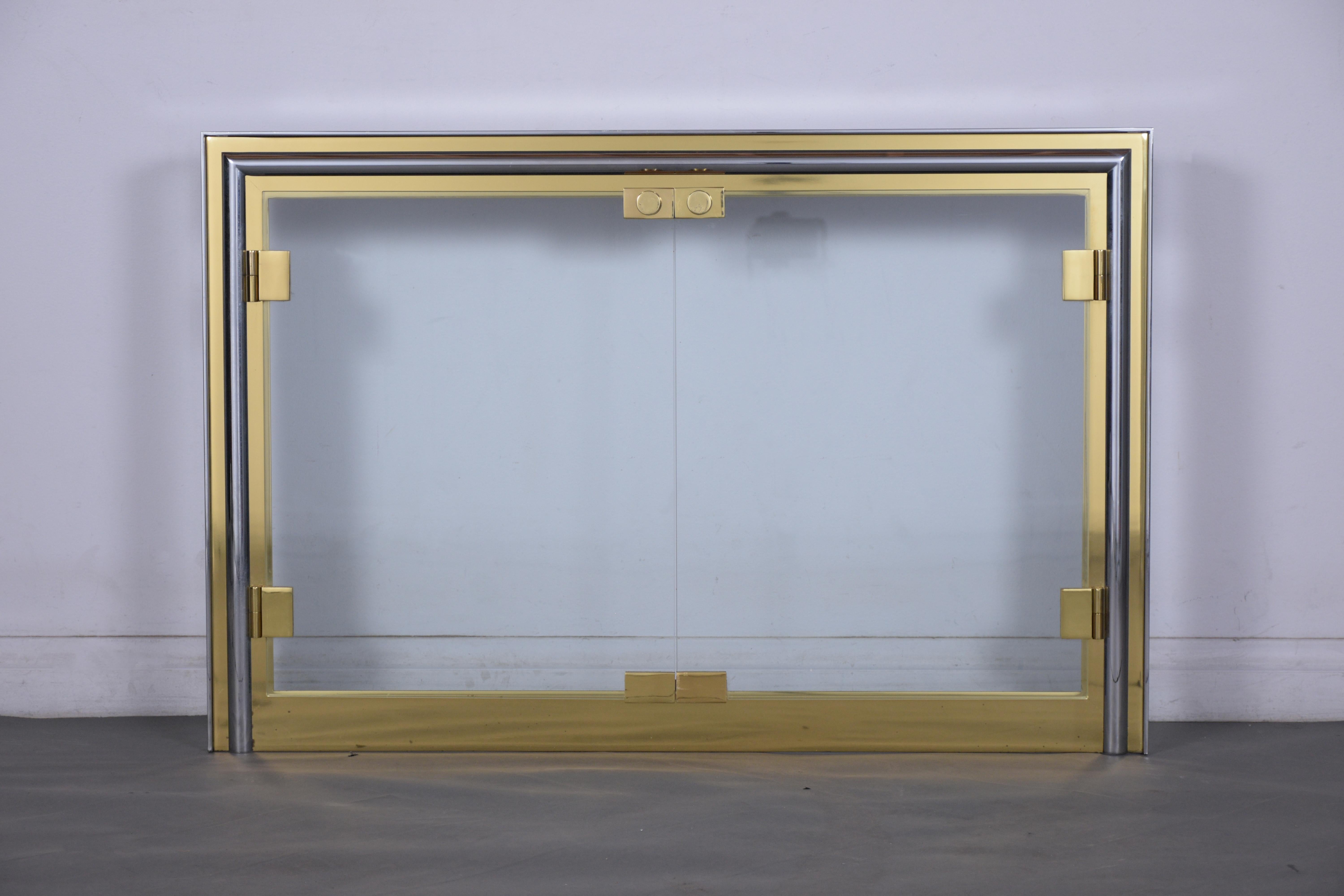 An extraordinary mid-century modern fireplace ornament hand-crafted out of brass and steel combination. This piece features a brass and chrome combination, with two-clear glass doors held by brass bracket hinges. This elegant modern glass screen is