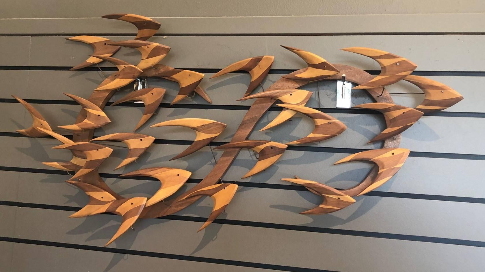 A very cool and unique midcentury wall sculpture of a school of fish swimming, circa 1960s. Each fish is handmade of what appears to be teak and walnut and is attached via a piece of metal wire. The piece is signed and is in very good vintage