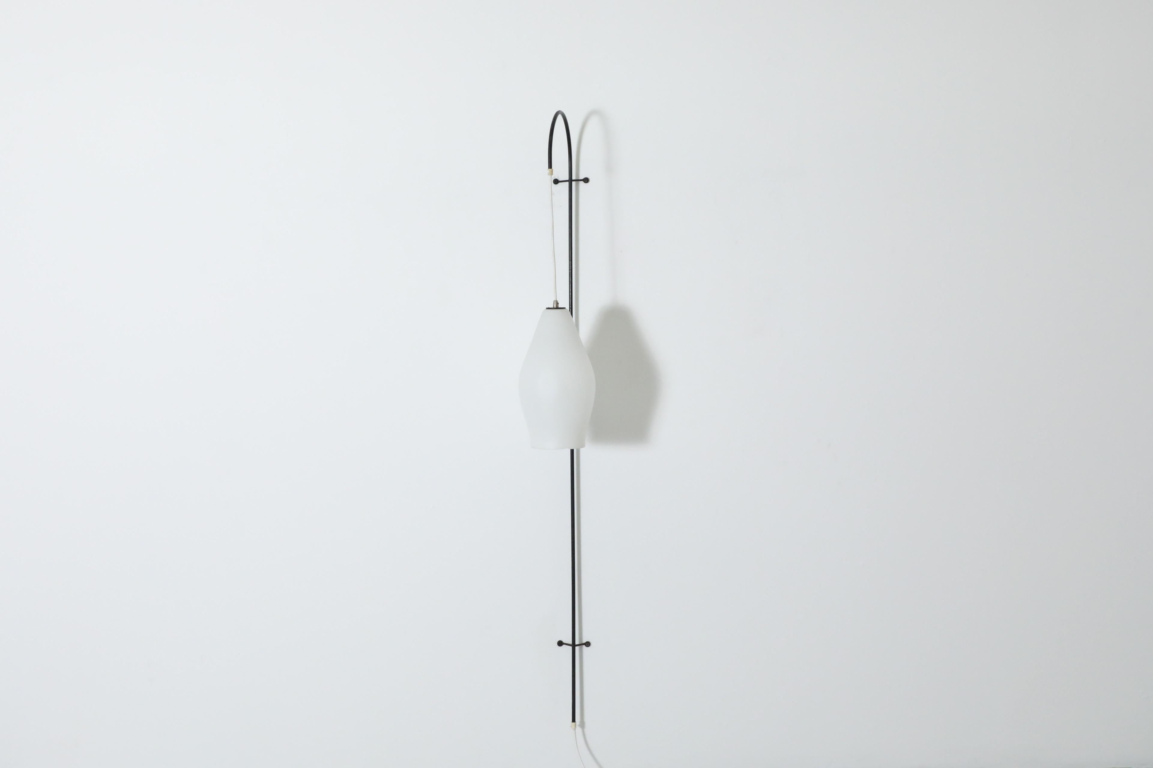 Mid-Century wall mounted fishing pole lamp with hanging milk glass shade pendant. Black metal wire frame with curved milk glass on a white power cord. This minimalistic wall lamp is perfect for a hallway space and provides sufficient directional