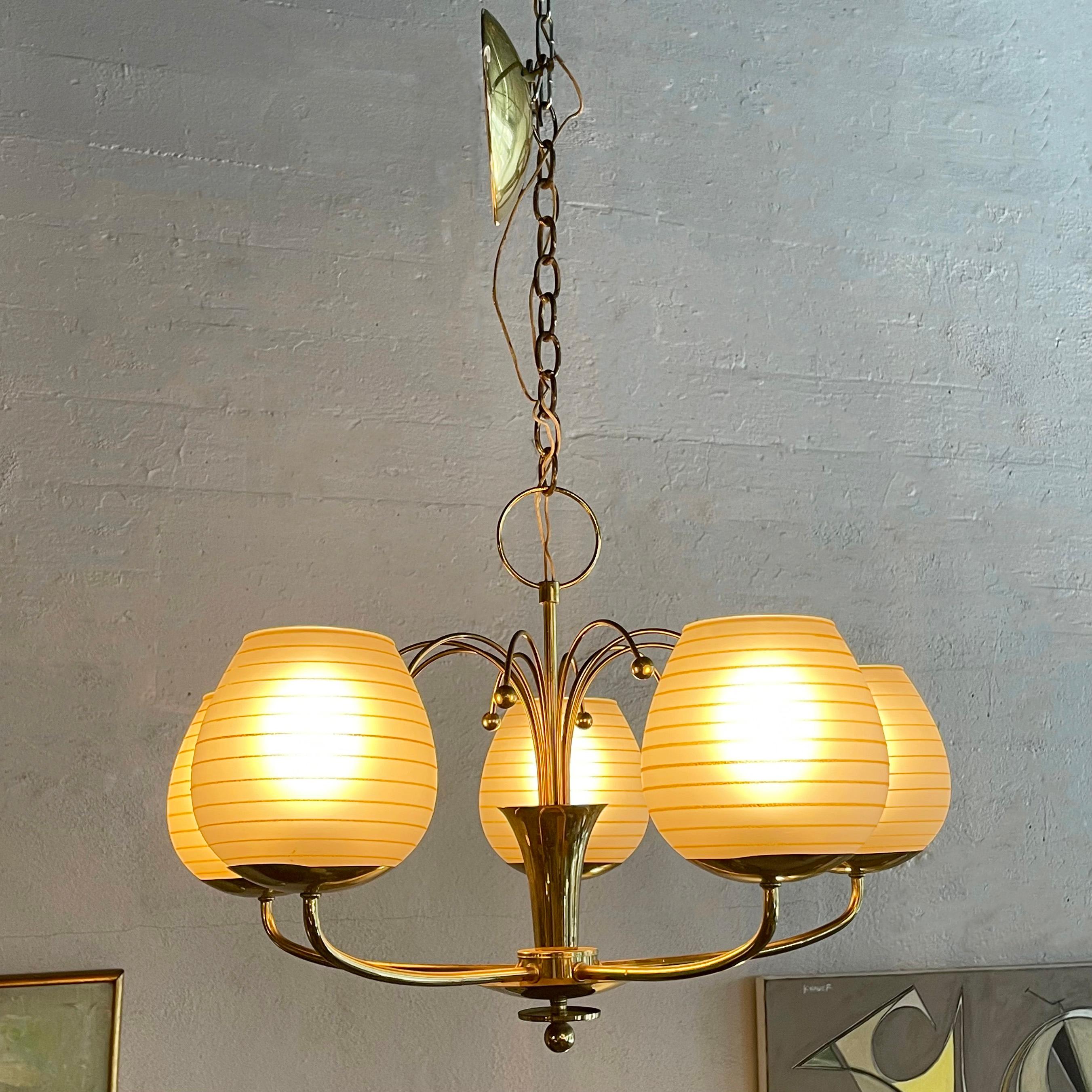 Elegante lampadario in ottone di metà secolo con 5 bracci estensibili sormontati da paralumi in vetro smerigliato a coste dorate aperti sulla parte superiore. Il lampadario presenta dettagli giocosi, come gli steli centrali che spuntano con le punte