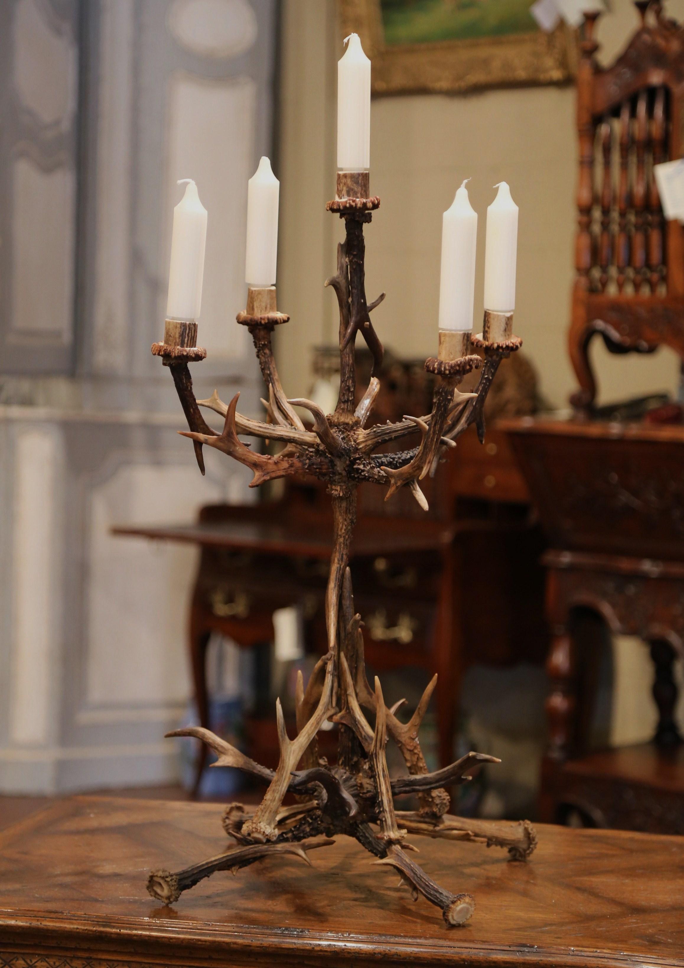 Decorate a side table or dining table at a ranch or hunting lodge with this elegant antler candelabra. Crafted circa 1960, the rustic, asymmetrical candleholder sits on four legs over the stem. The candlestick features five arms each holding a