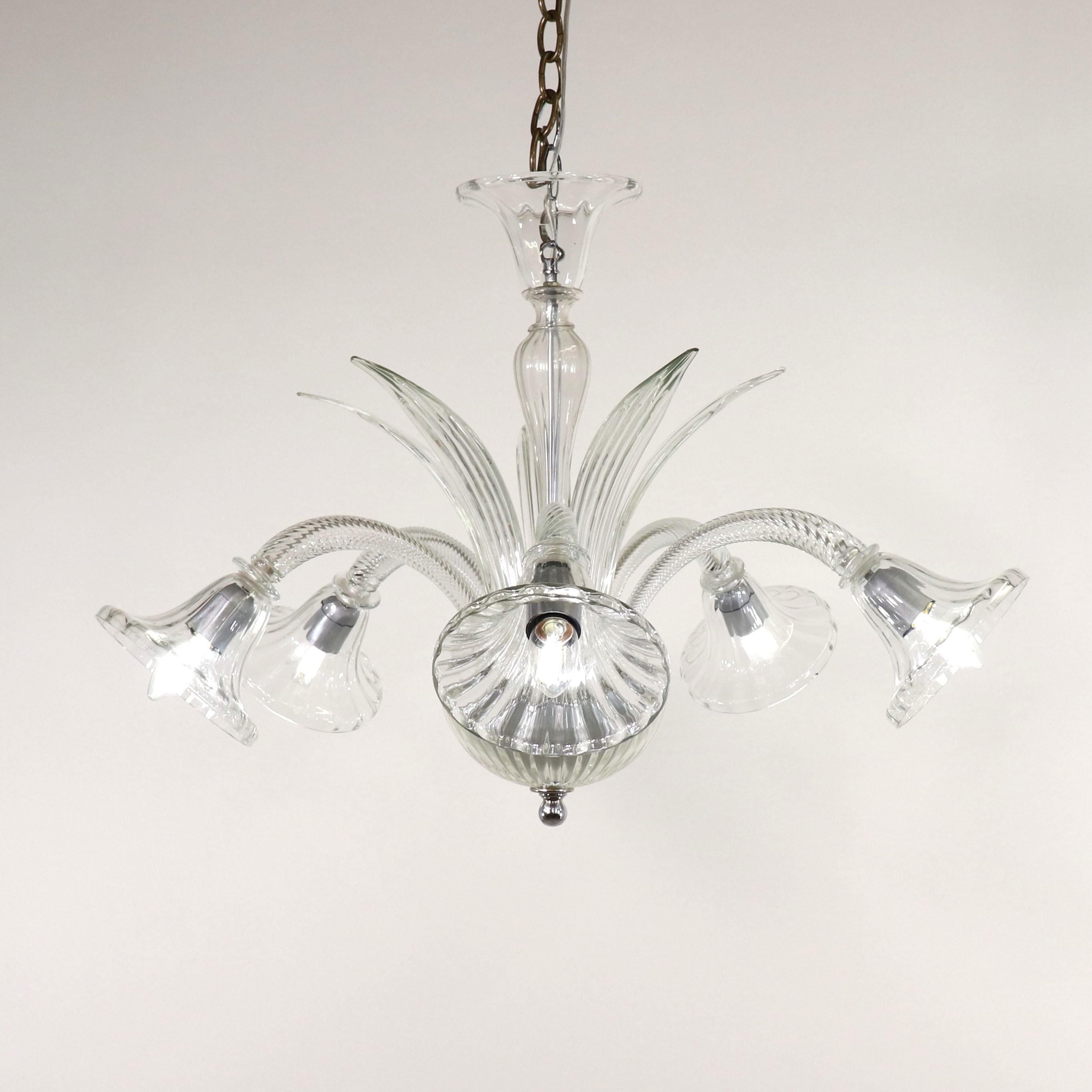 This tasteful mid-century modern Murano chandelier has five scroll arms, a bulbous center column with sprouting leaf details, and scalloped rims. The body and arms of this piece are made of clear, colorless Venetian glass. The glasshouses on the
