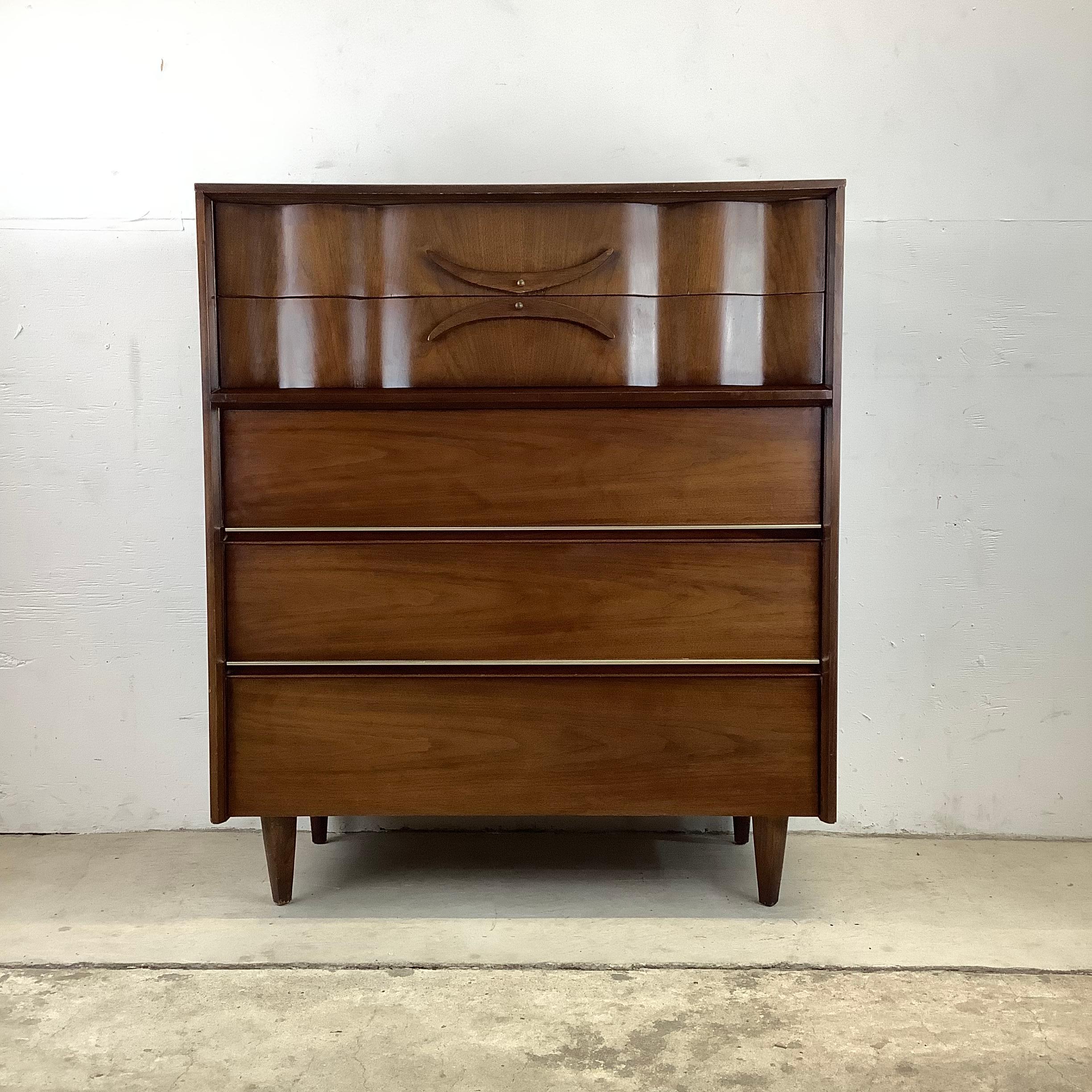 This stylish highboy dresser features the perfect mix of Mid-Century Modern style, vintage walnut finish, and spacious drawers for plenty of bedroom storage. Unique sculptural wooden handles, tapered legs, and clean modern lines add to the charm of