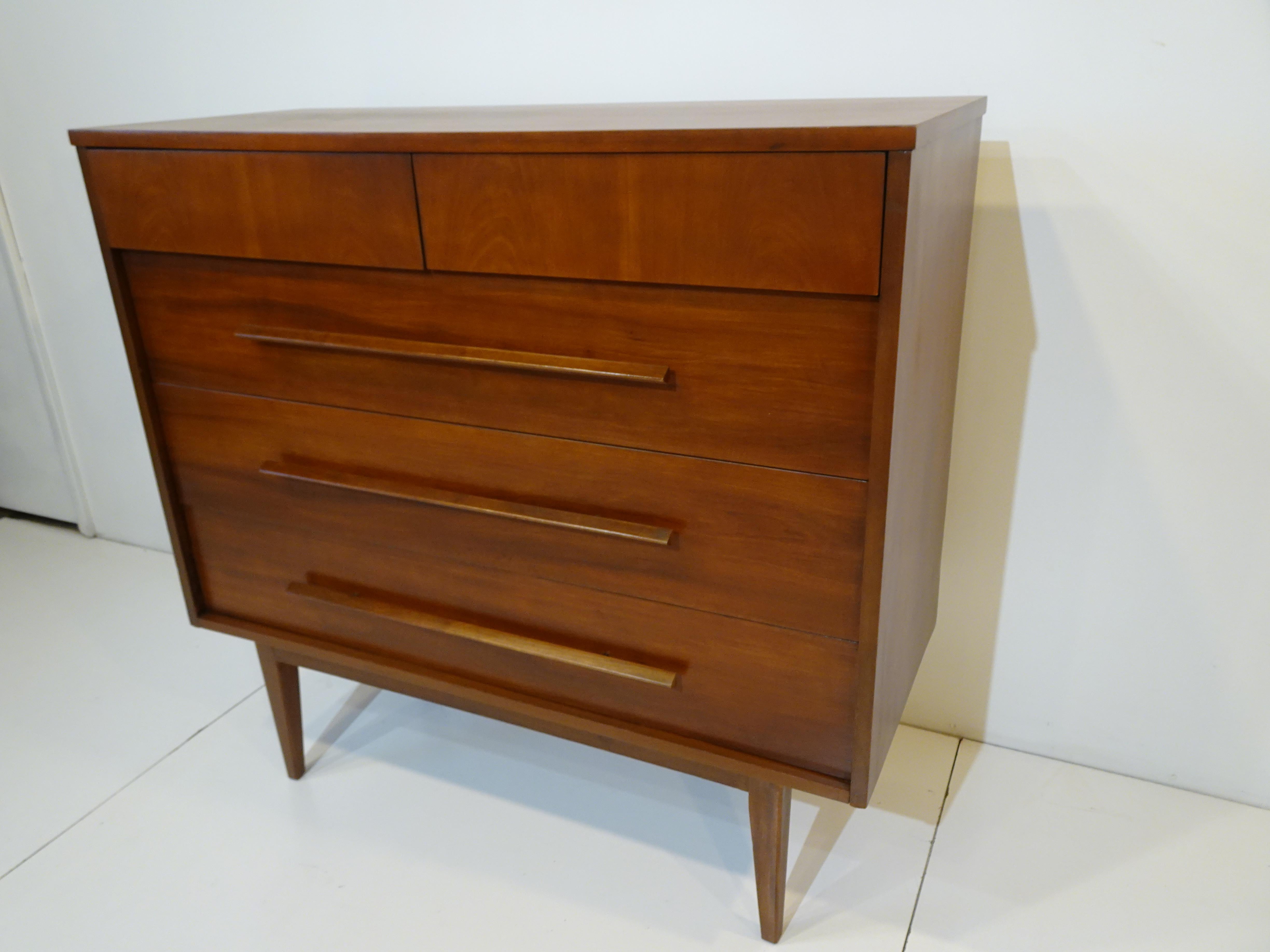 A nice dark walnut mid century dresser with two thin smaller upper drawers and three larger lower drawers with matching long streamline pull handles. A very clean design that works well with many different decors having plenty of storage and would