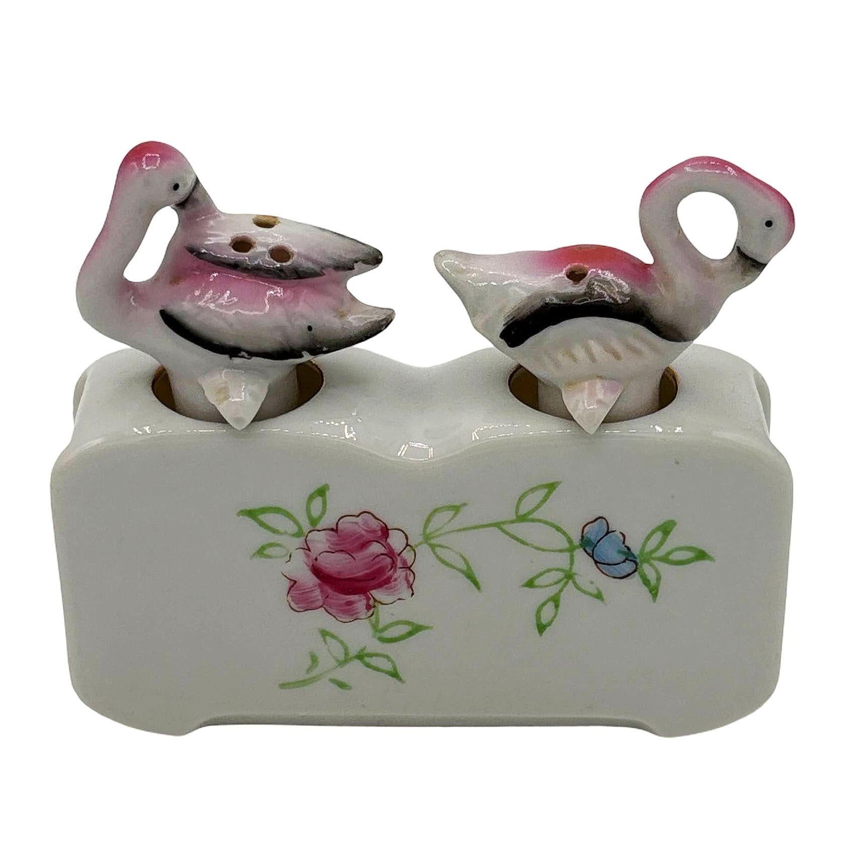 Mid-century pink and green ceramic flamingo tabletop salt & pepper with a holding base by Express. The set features two beautifully detailed pink flamingos in white with a holding base that has a decorative floral hand-painted along the front.

Made