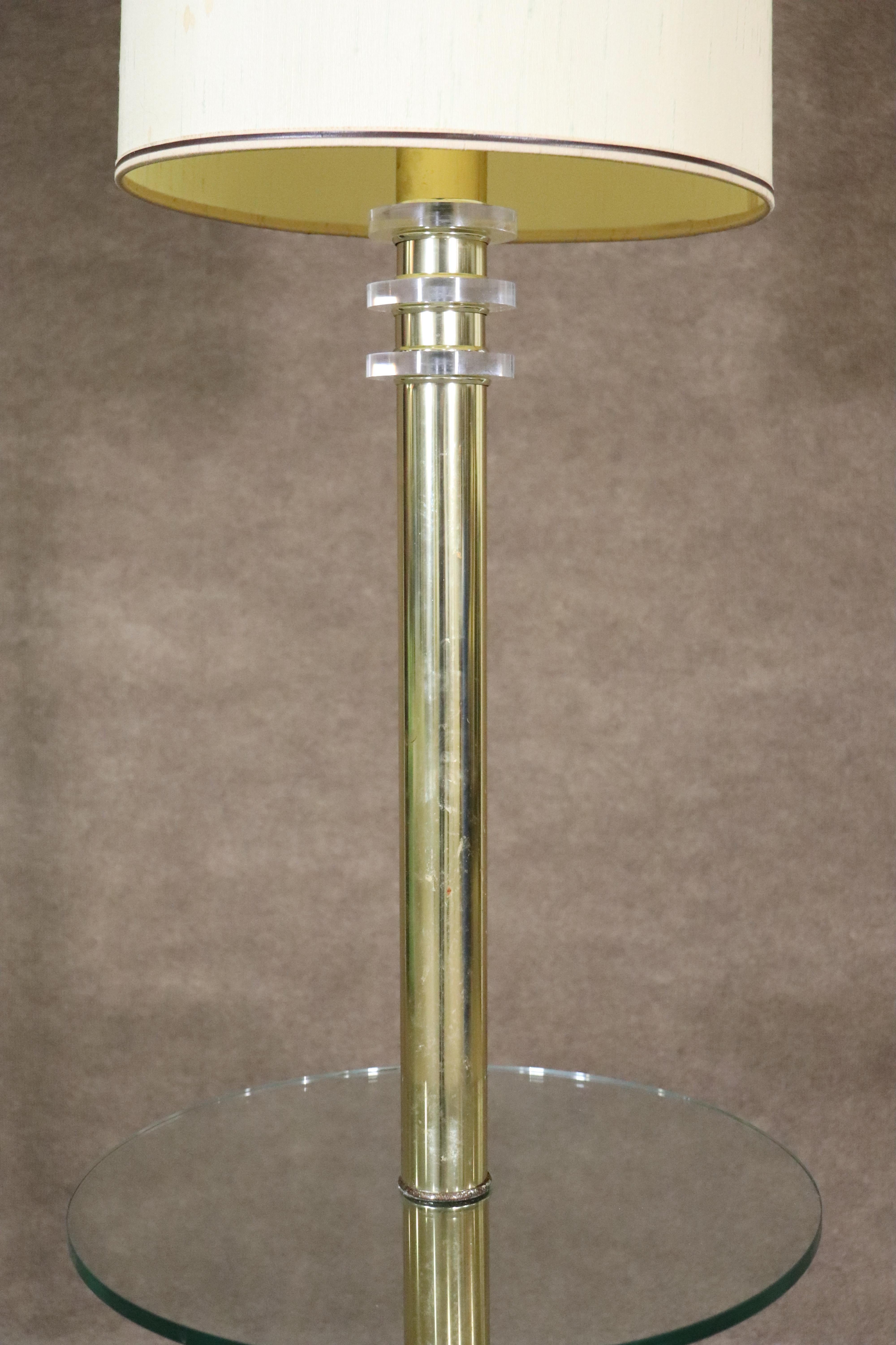 Tall floor lamp in polished brass with round glass table shelf. Accenting lucite discs sit under the round shade.
Please confirm location NY or NJ