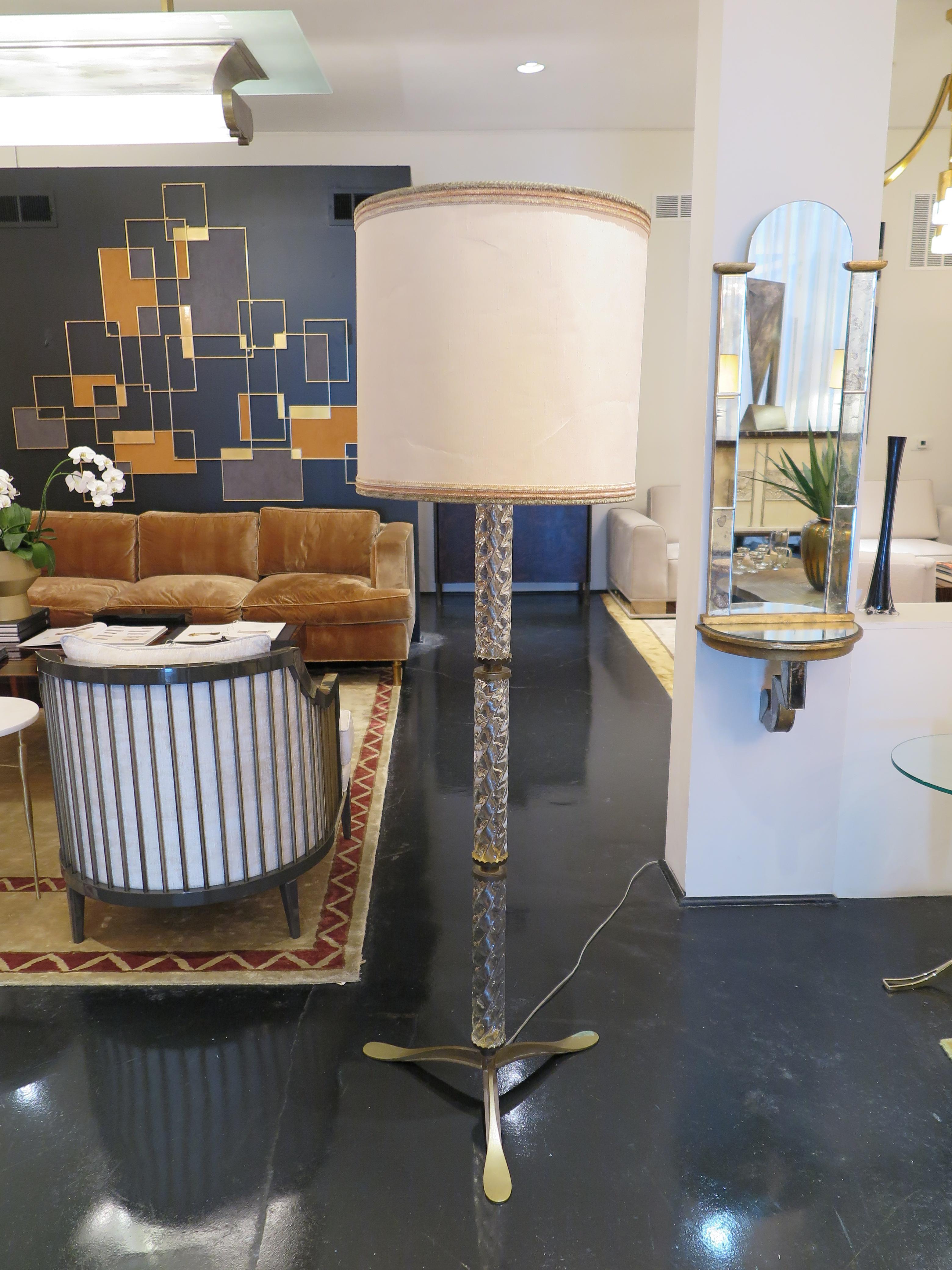 This mid-century floor lamp features three clear Murano glass twisted cylinders with scalloped dividers in antiqued brass. Three legged base in antiqued brass. The original shade is in silk with 3 piece colored trim. This piece is in original