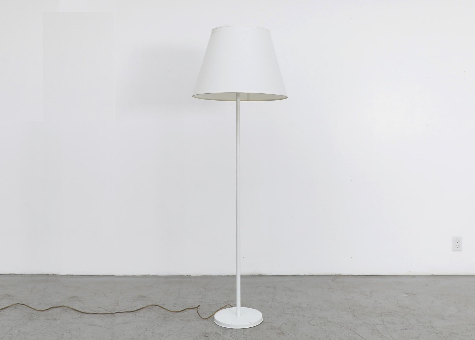 Mid-Century standing floor lamp with white enameled metal stem and base, circa 1960. Newer white linen tapered drum shade. In original condition with visible wear consistent with its age and use.