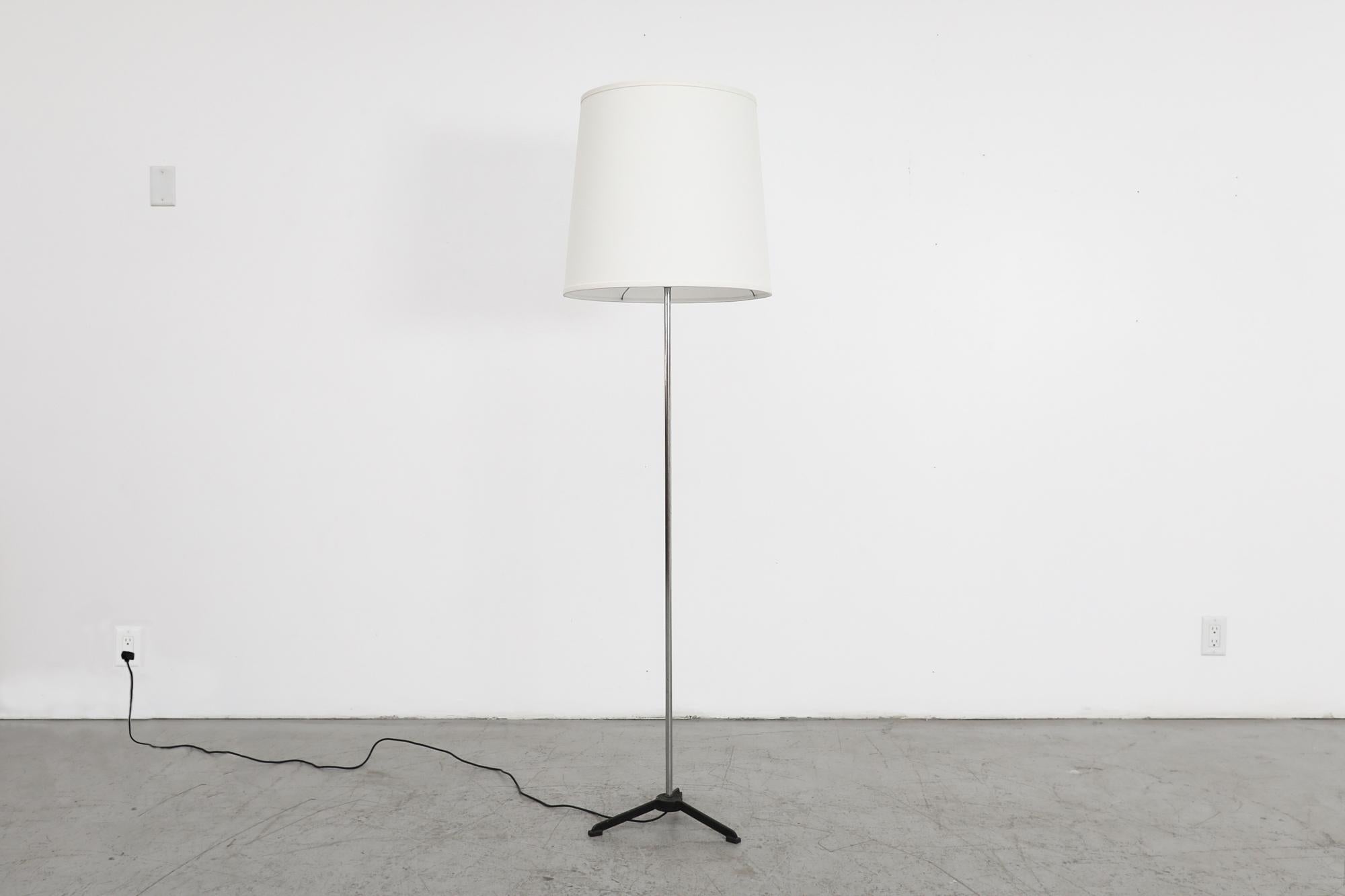 Lampada da terra di metà secolo con stelo cromato e base a treppiede ispirata a Matego smaltata di nero. Paralume a tamburo conico in lino bianco più recente. Utilizza una lampadina standard a base media E26/E27. In condizioni originali, con