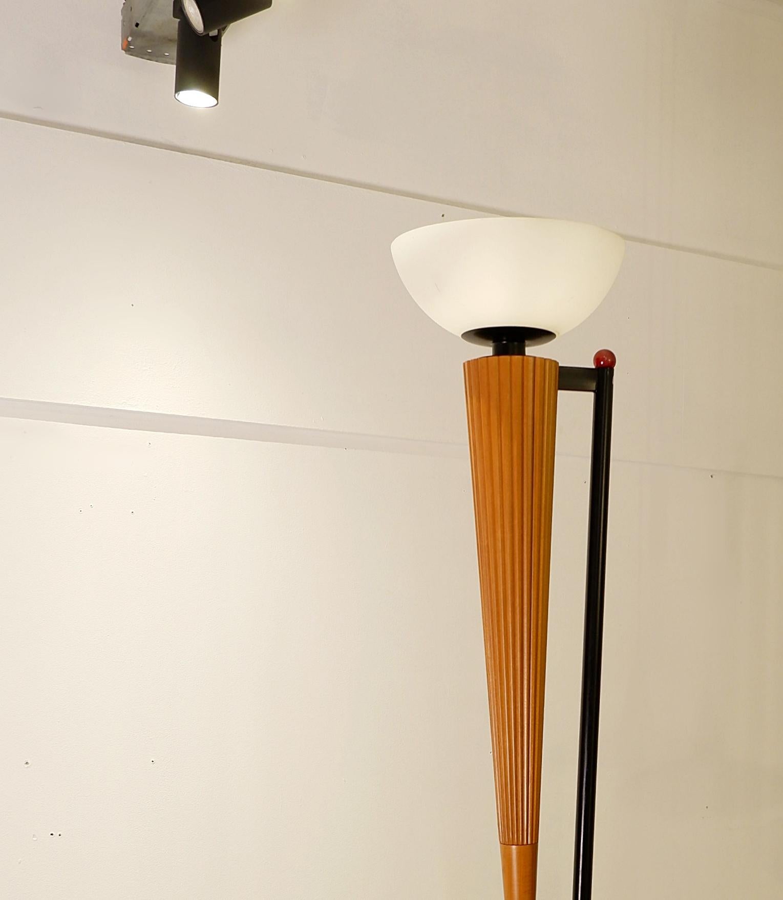Tall Floor lamp in the style of Italian Designer Ettore Sottsass. The lamp is resting on a large wooden base, and the semi-spherical lightbulb is perched on a long sharp wooden cone. 
