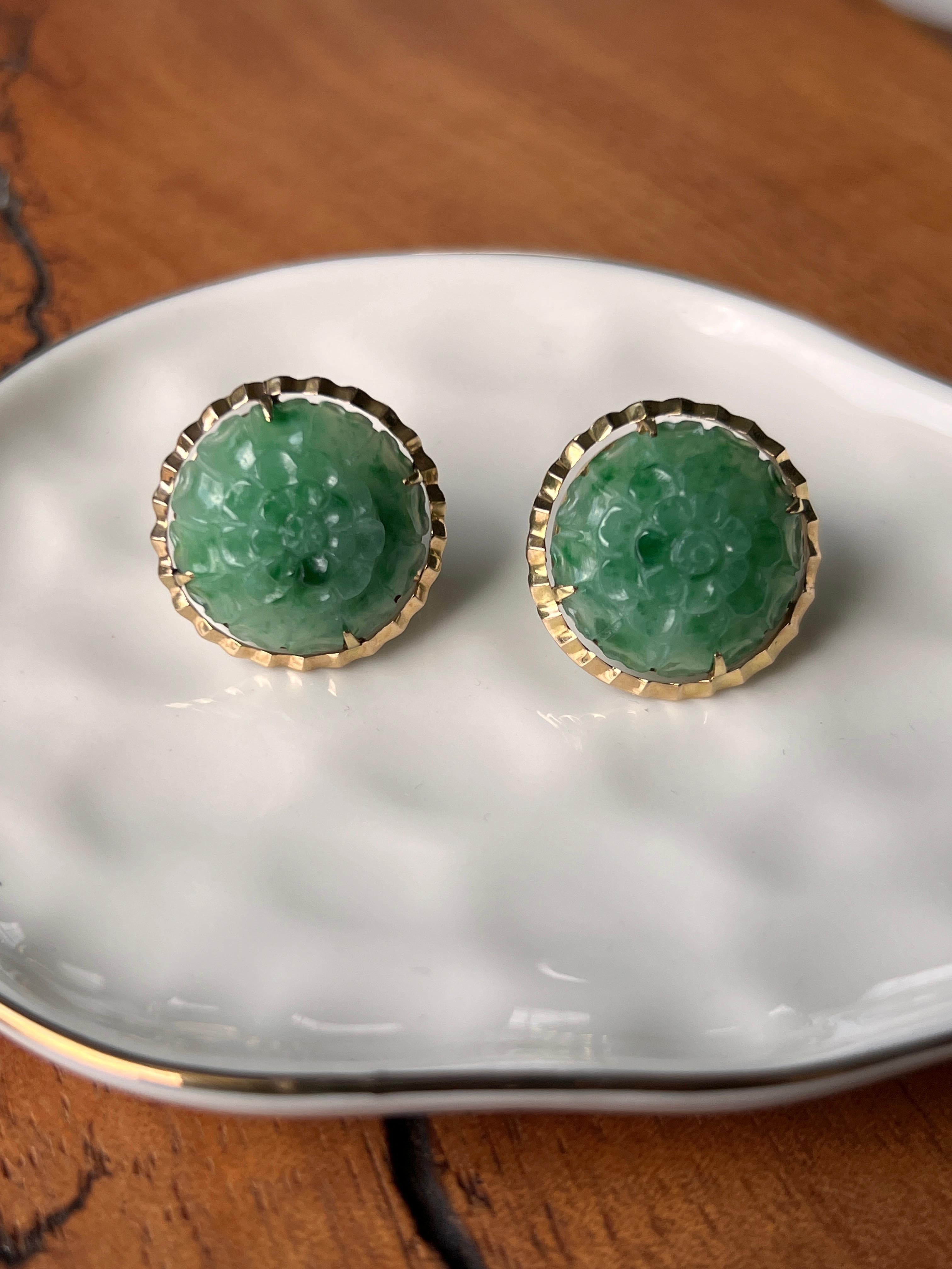 Une paire de boucles d'oreilles en or jaune 14 carats du milieu du siècle dernier, chacune sertie d'une jadéite ronde sculptée mesurant environ 17,94 mm. La jadéite présente une riche couleur verte et une sculpture florale complexe, créant une pièce