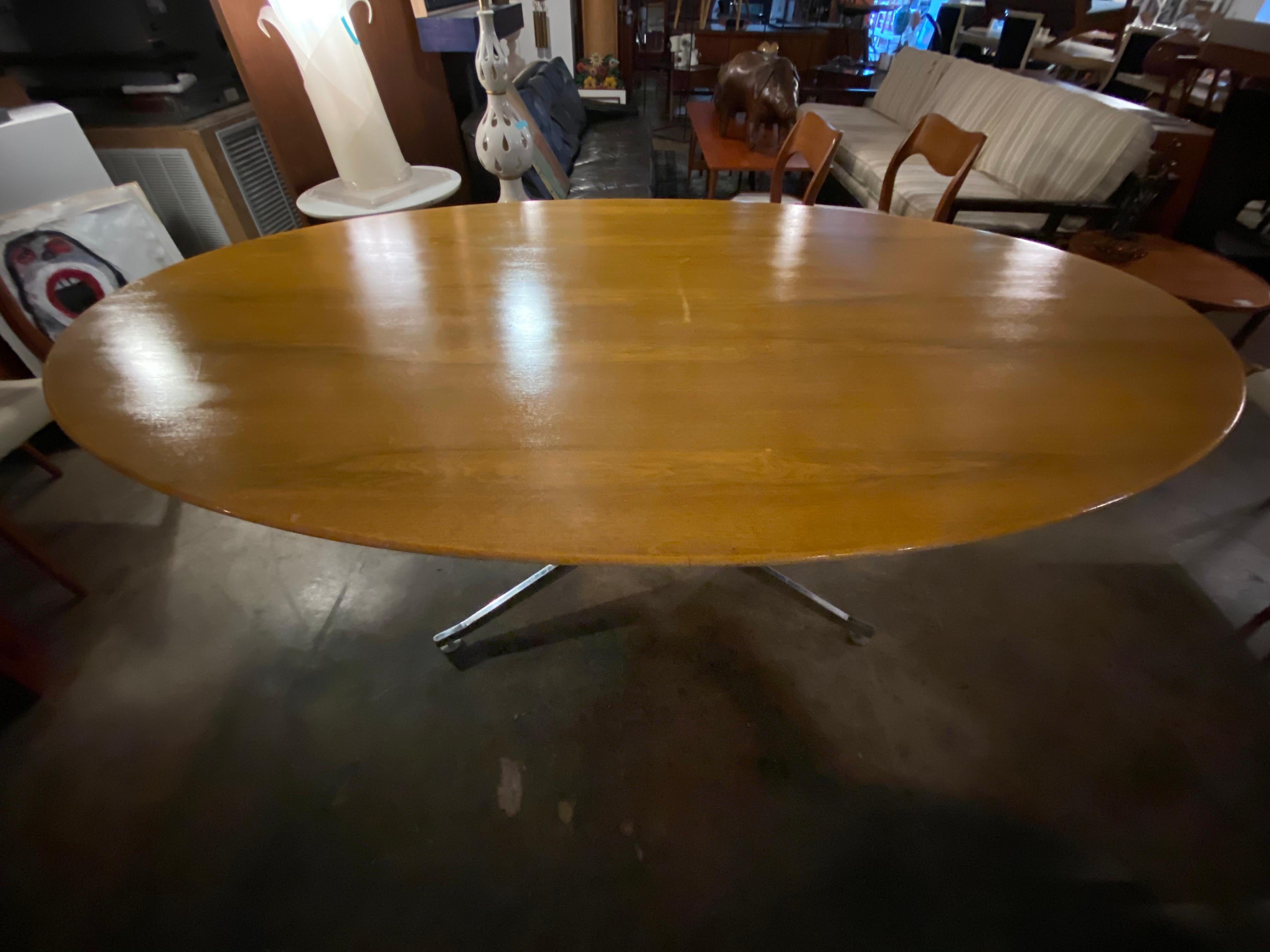 Mid-Century Modern table designed by Florence Knoll. In good condition, this vintage table is oval shaped, walnut wood top with a chrome base, and can easily seat eight. This large table is beautiful as a dining table or can be used as an office