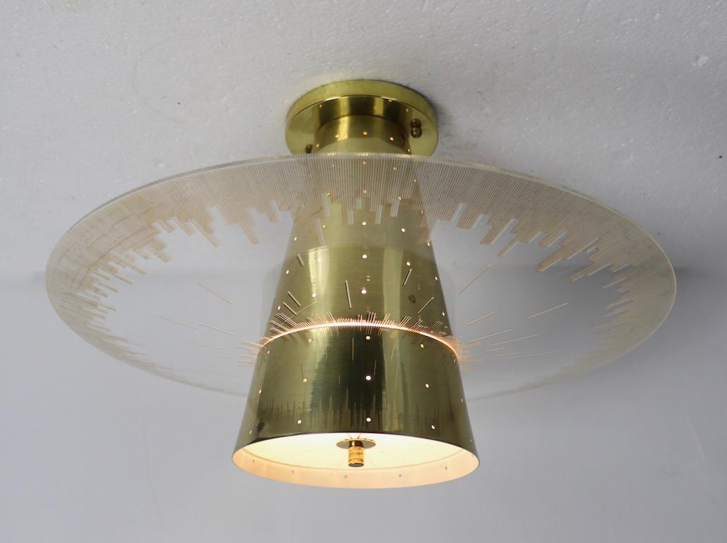 Chic Mid-Century Modern chandelier by Moe Light. This fixture has a pierced brass center cone which supports the glass ring shade. The ring shade has a city skyline motif edge; the center cone has a clip on glass disk shade. The fixture is in very