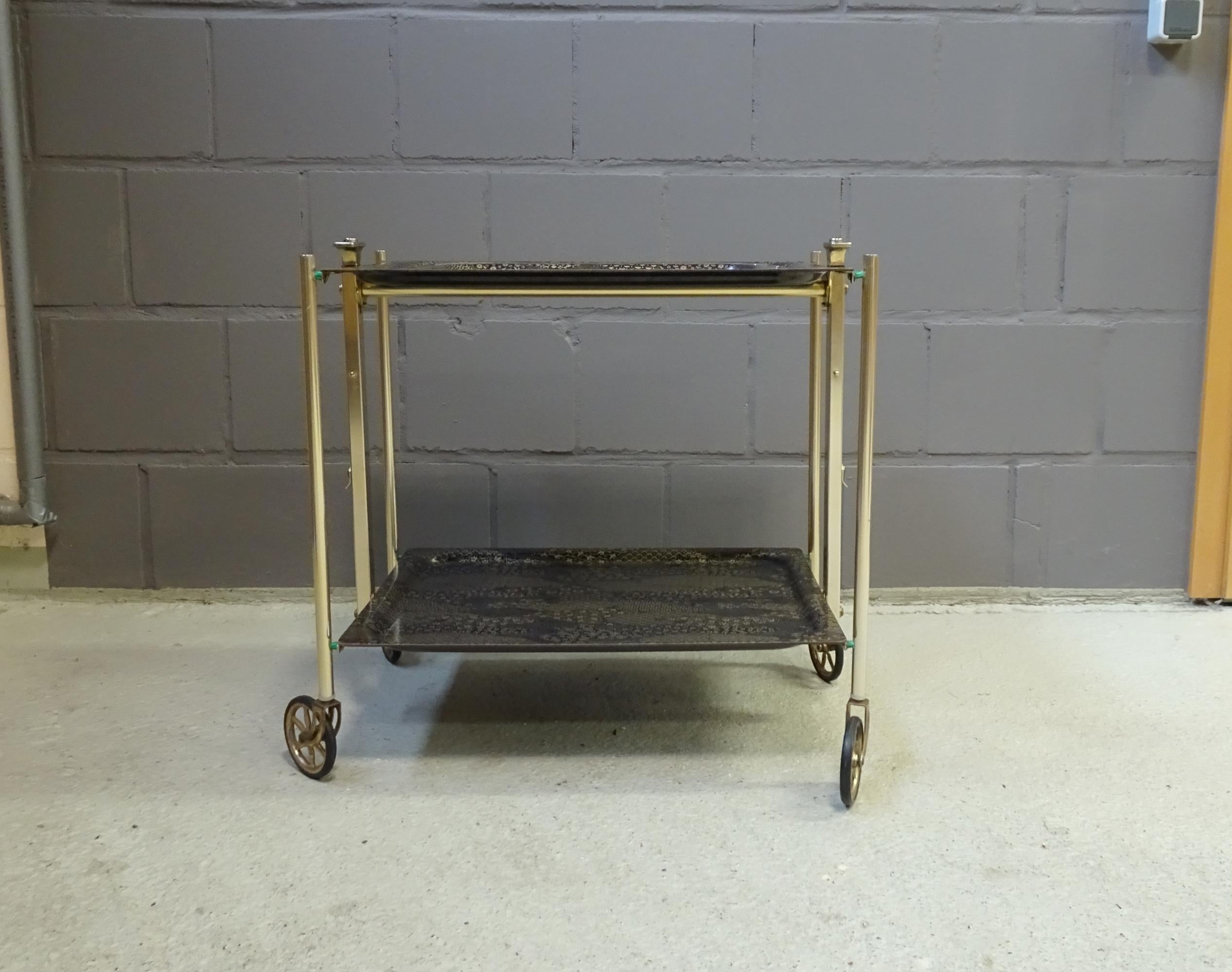 Foldable serving trolley, black and gold dinette, noble bar trolley, trolley, midcentury side table, textable serving table.

Noble Dinett serving trolley from the 1960s-1970s with two shelves on wheels. This version in black and gold-colored