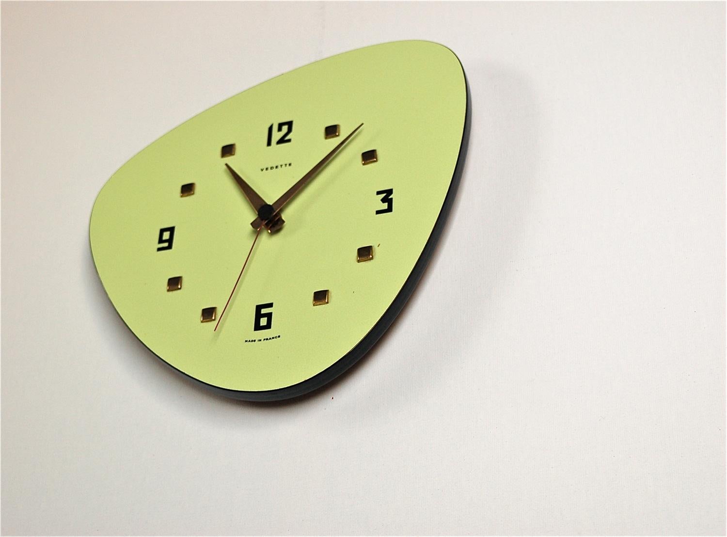 Mid-Century Modern wall clock by French manufacturer Vedette. The design is quintessentially 1950s with its organic shape and pale green colored formica front with black edging. The makers name is featured at the top of the dial and made in France