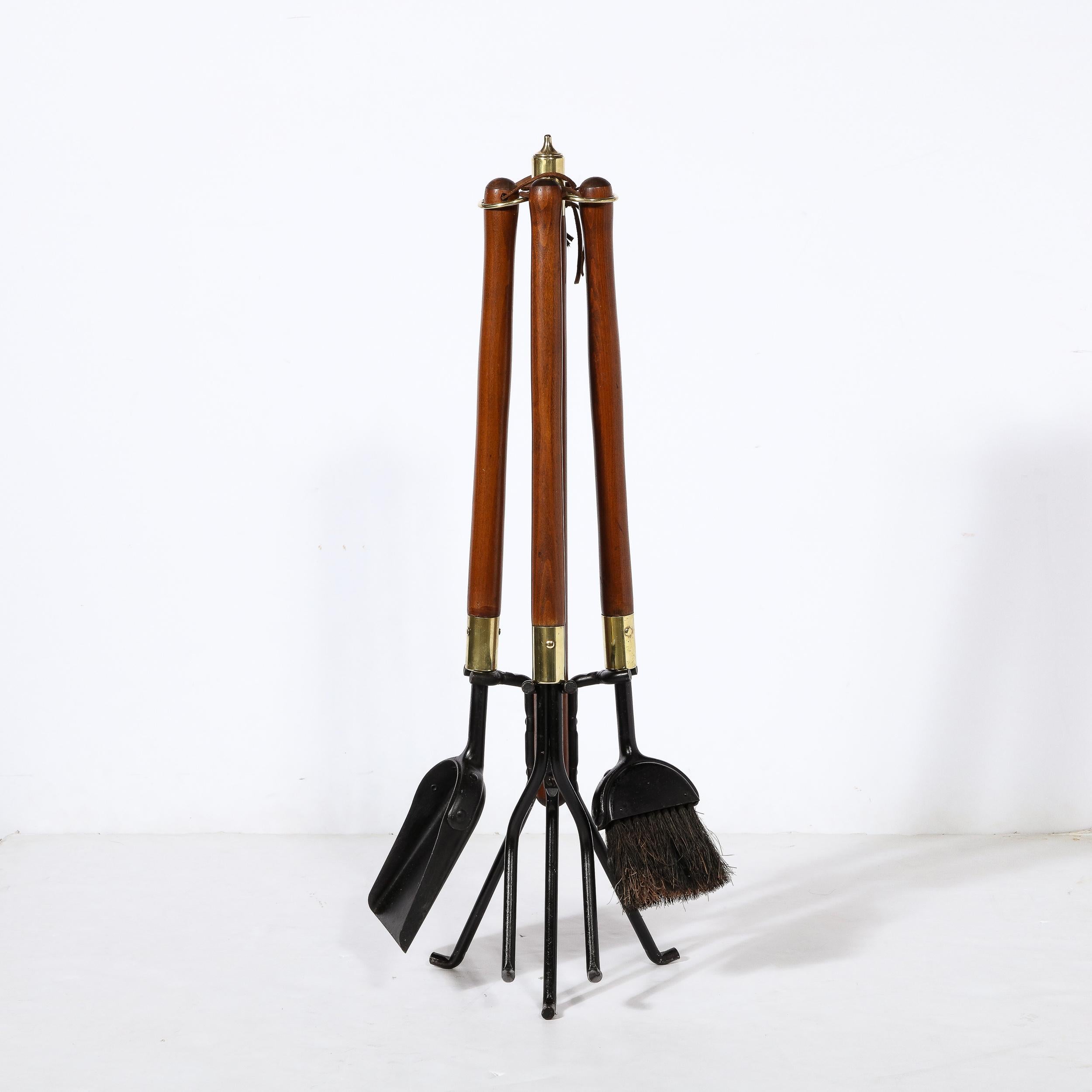 This refined Mid-Century Modern four piece fire tool set was realized in the United States, circa 1960. It features a poker, brush and shovel with hand rubbed walnut handles offering rounded subtly protuberant ends ends, and black enamel bottoms