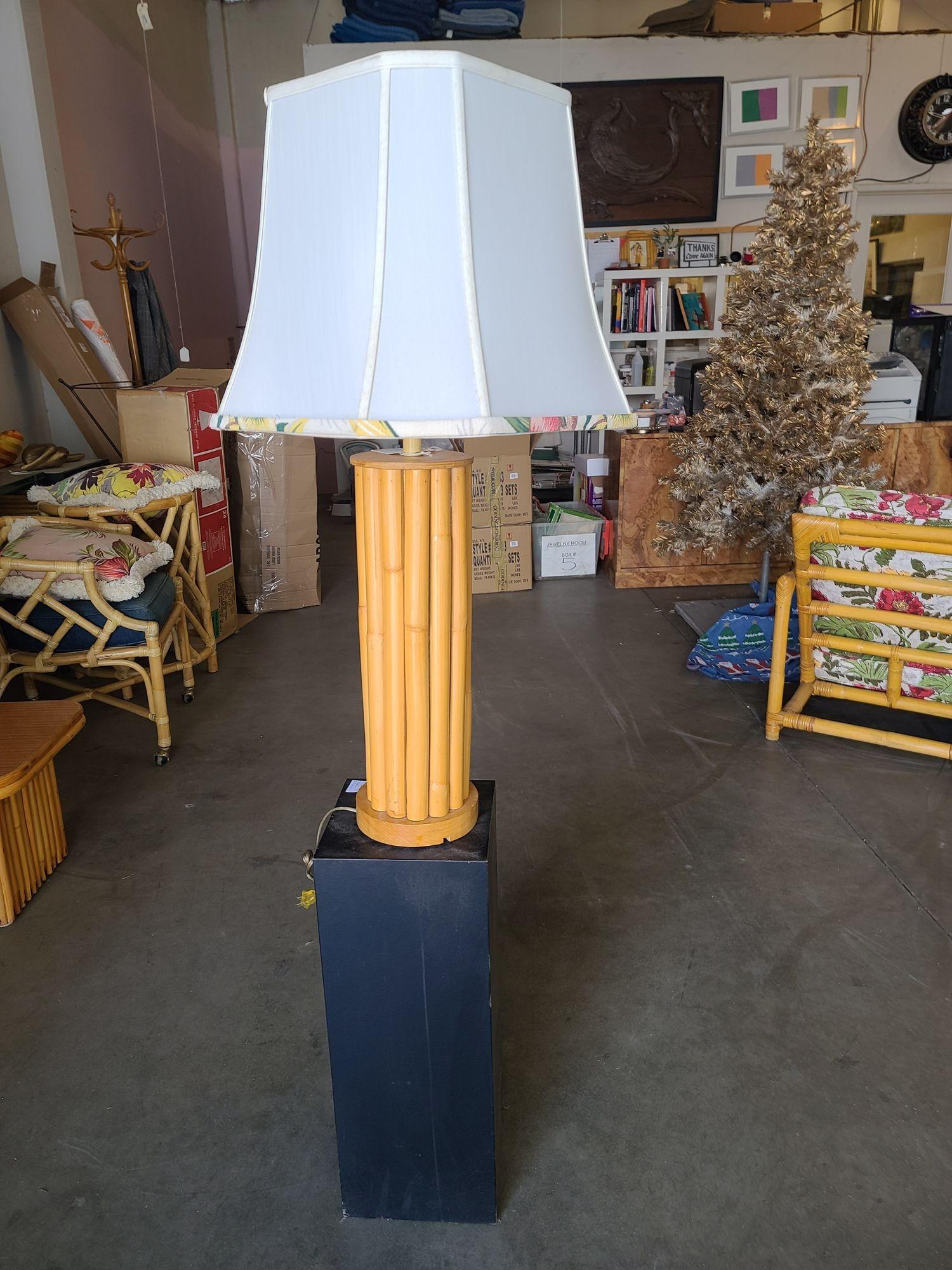 Restored mid-century rattan table lamp featuring 14 vertically stacked rattan poles fixed between two bleach blond teak caps with a brass 120 US socket.

The lamp comes with a white fabric shade featuring a tropical pattern fabric along the bottom