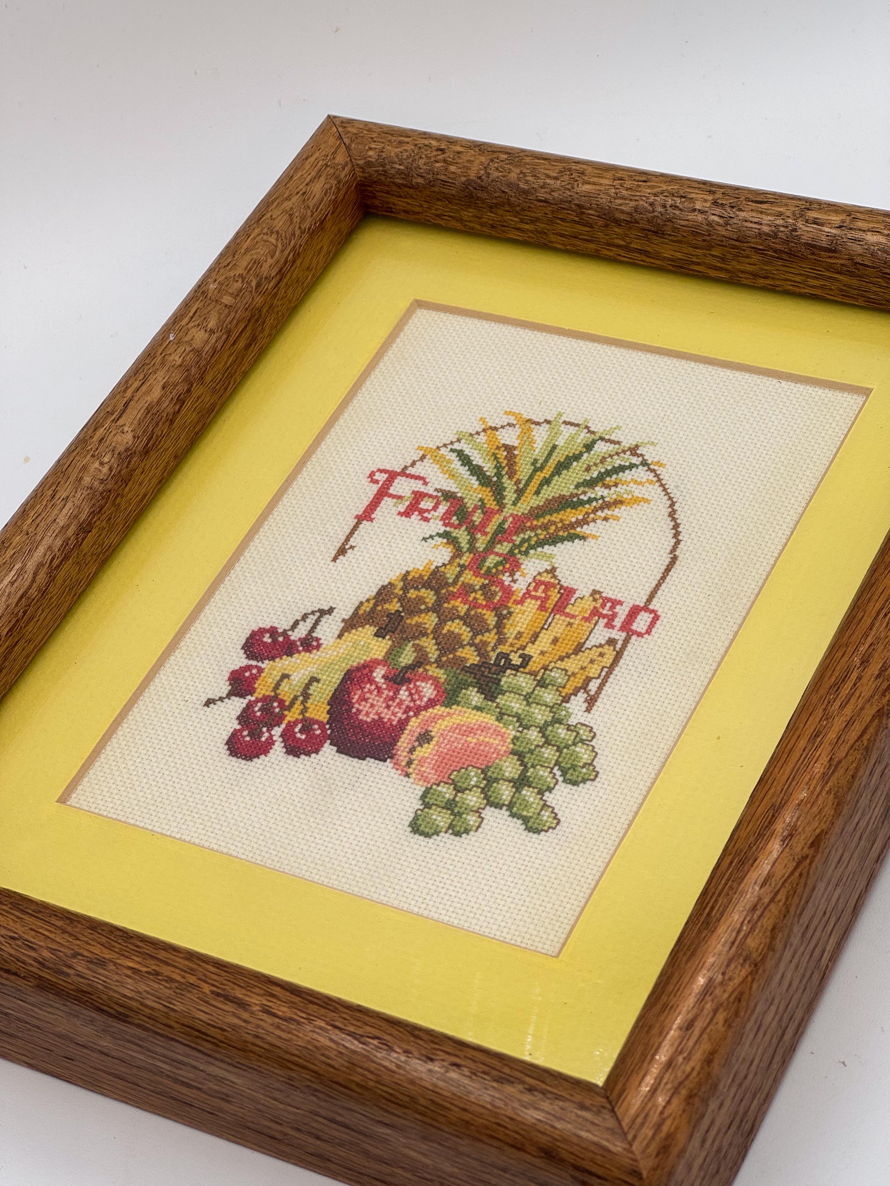 Une œuvre d'art à l'aiguille des années 1970, vibrante et charmante, représentant un arrangement coloré de fruits avec le texte ludique 