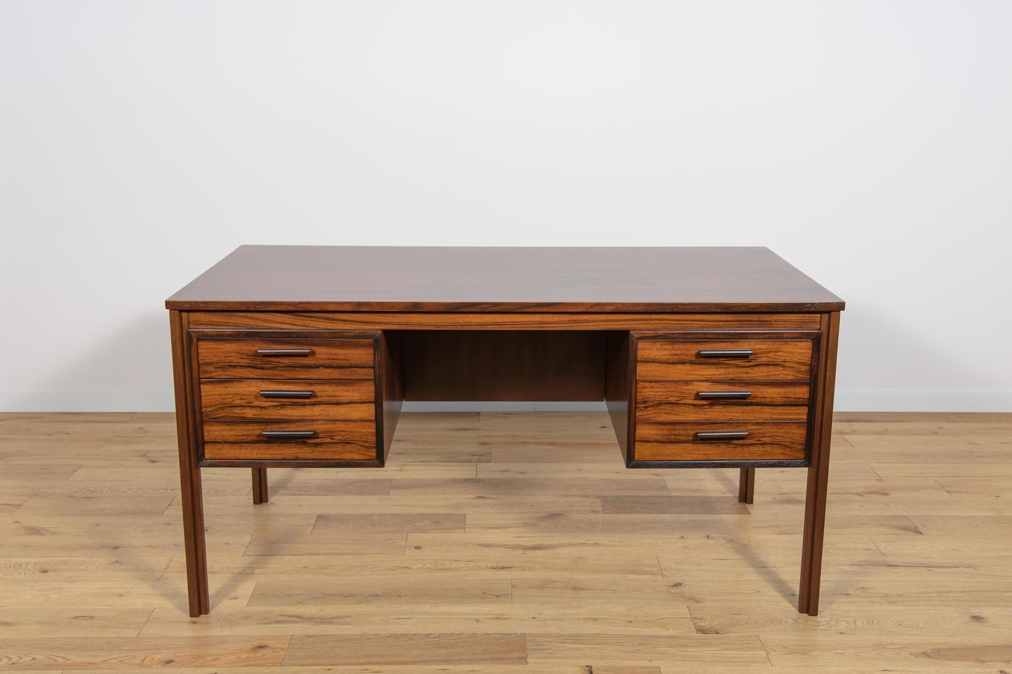 Dieser Schreibtisch wurde in den 1960er Jahren in Dänemark hergestellt. Der Schreibtisch ist aus Palisanderholz gefertigt und steht dank der fertigen Rückwand mit offenem Stauraum für Bücher freistehend. An der Vorderseite befinden sich zwei Module