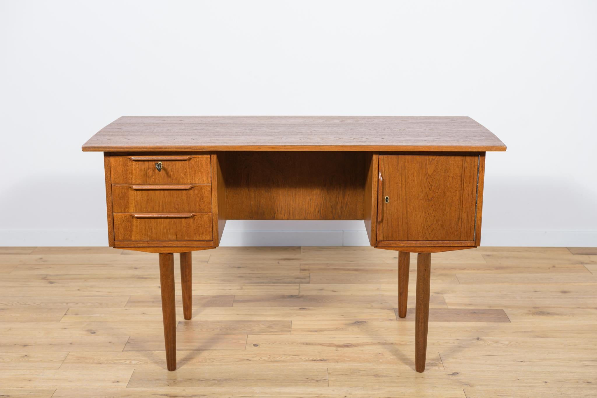 This desk was made in Denmark in the 1960s. It was made of teak wood with contoured handles. It consists of two modules, on the left there are three drawers, on the right there is a lockable cabinet with shelves. There is a bookshelf in the back.