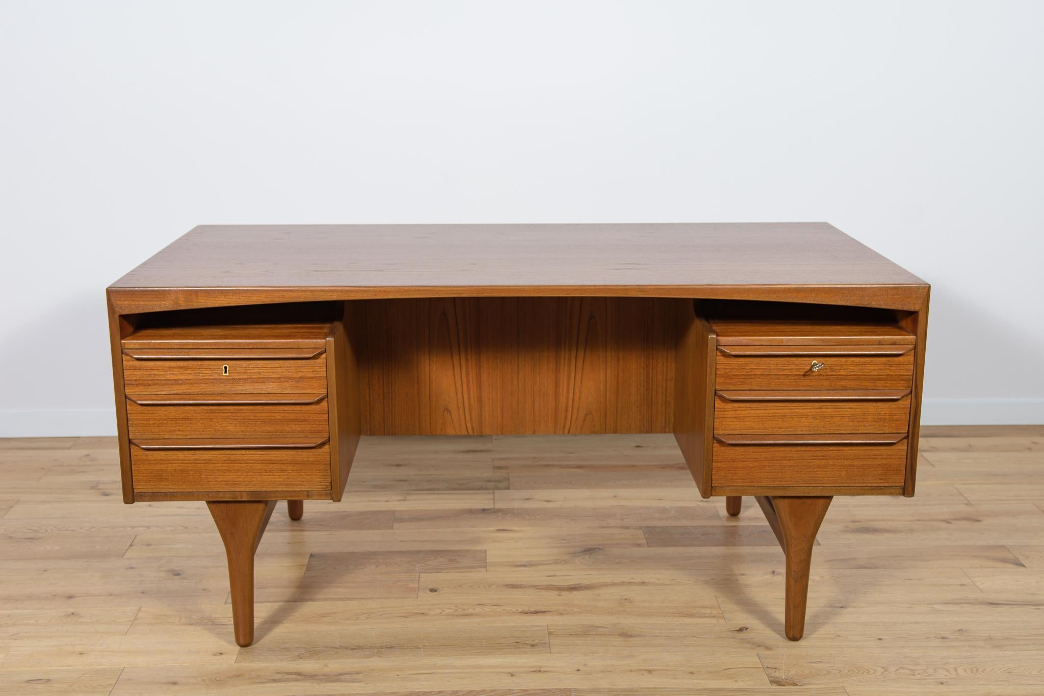 The desk designed by Valdemar Mortensen, produced in Denmark in the 1960s. The desk is made of teak wood and is free-standing. There are two modules at the front - three drawers each. At the front there is a bookshelf and a lockable cabinet. The