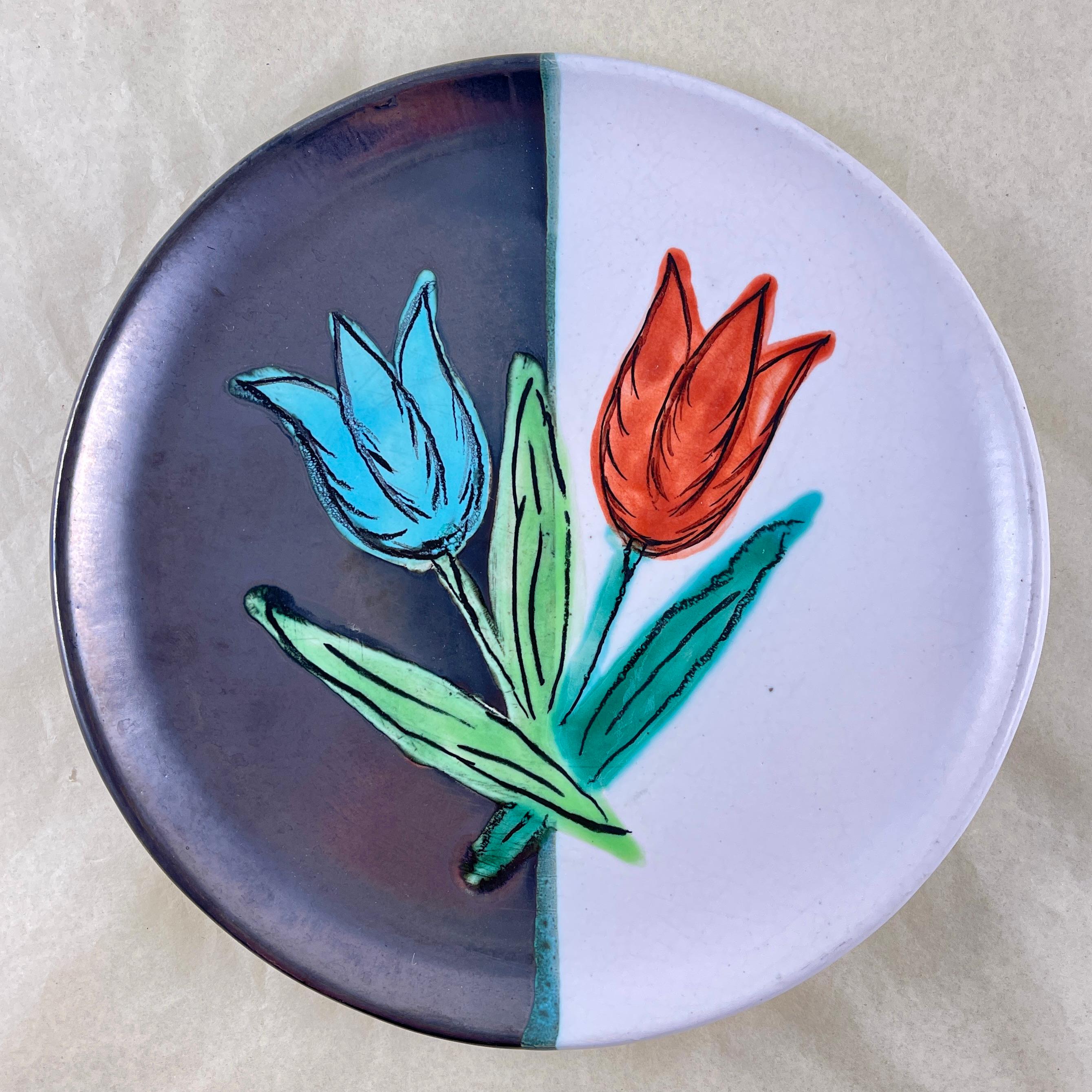 
From the Atelier Cérenne à Vallauris in France, a hand made pottery Tulip plate, circa 1940-1950.

The plate is finished in a matte glazing of half black and half white, with a pair of raised, glossy glazed tulips painted in a complimentary color