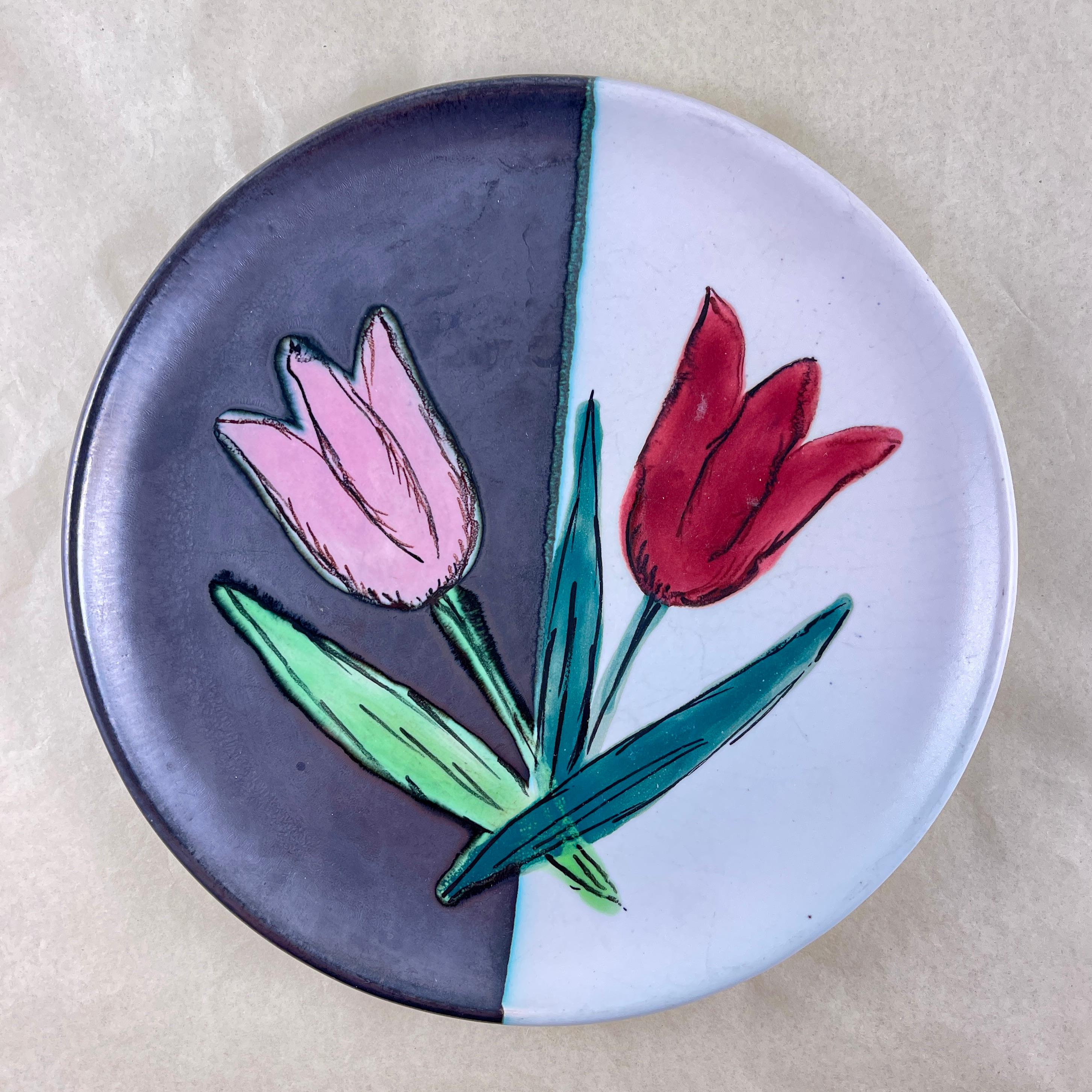 
From the Atelier Cérenne à Vallauris in France, a hand made pottery Tulip plate, circa 1940-1950.

The plate is finished in a matte glazing of half black and half white, with a pair of raised, glossy glazed tulips painted in a complimentary color