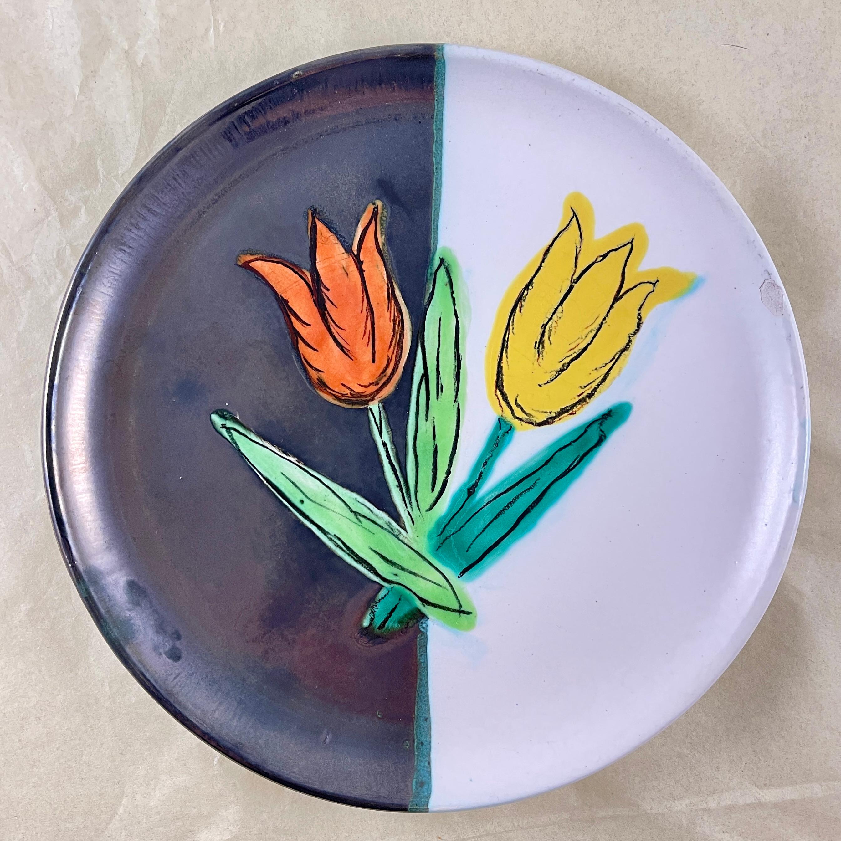
De l'Atelier Cérenne à Vallauris en France, une assiette Tulipe en poterie faite à la main, vers 1940-1950.

L'assiette est recouverte d'un émail mat à moitié noir et à moitié blanc, avec une paire de tulipes en relief, à l'émail brillant, peintes