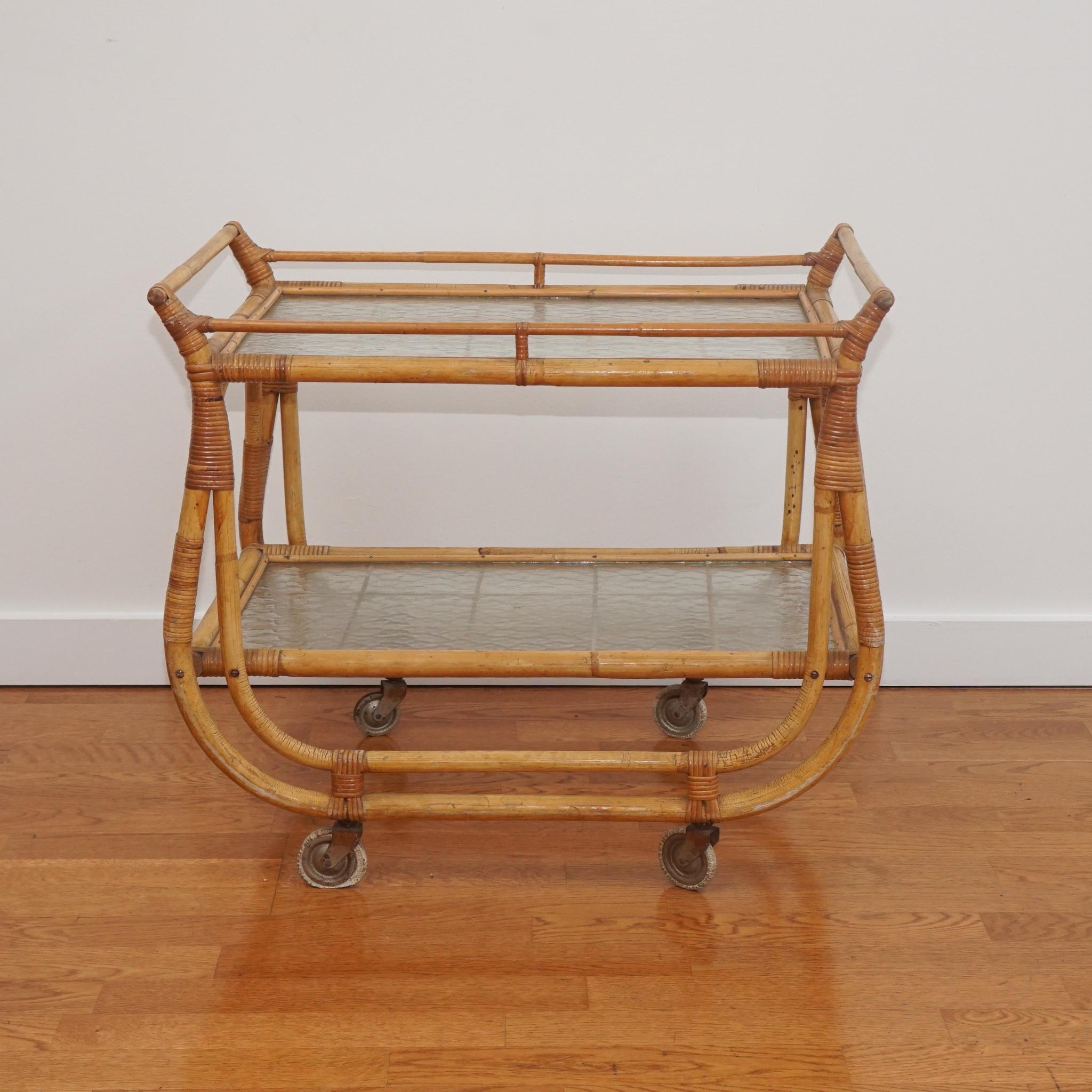 This Mid-Century Modern French bamboo and rattan bar cart is from the 1950s. 
Designed with two grid-patterned glass shelves, the stylish frame is in very good condition and exhibits the warm patina and variation of color that comes with age. The