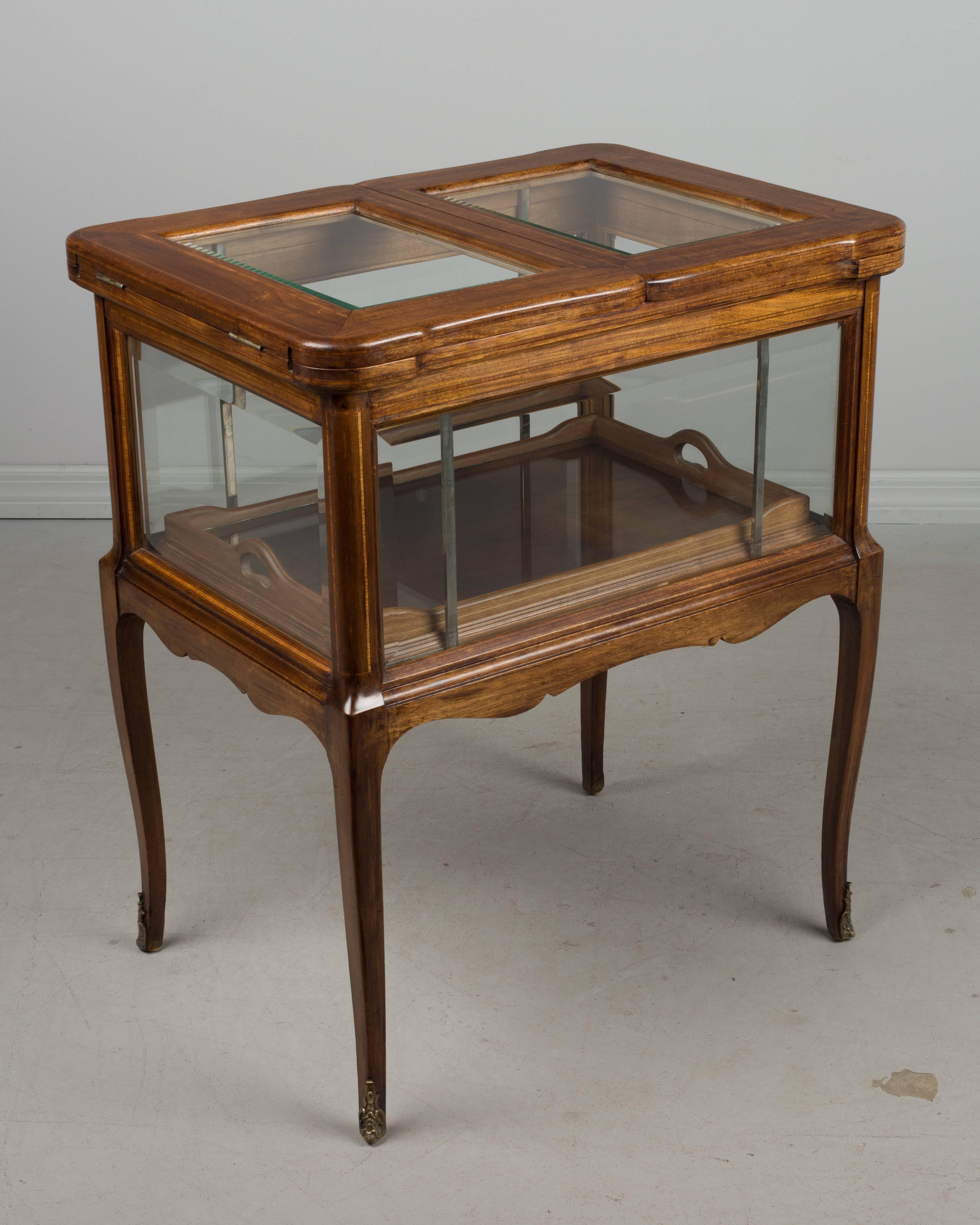 A midcentury French bar cabinet made of mahogany with beveled glass and marquetry inlay. Unusual design with a mechanism that raises the bottom interior when the top is hinged open. A removable glass serving tray with wood frame rests inside ready